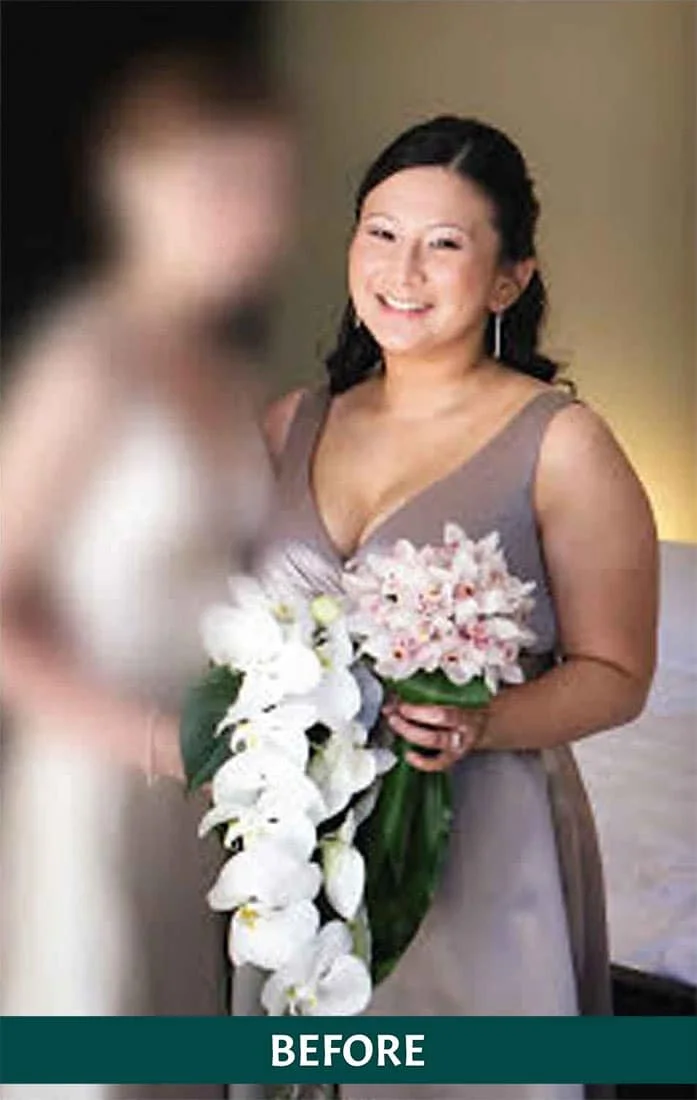 A woman in a gray dress smiling and holding a bouquet of white and pink flowers, with another person blurred in front of her.