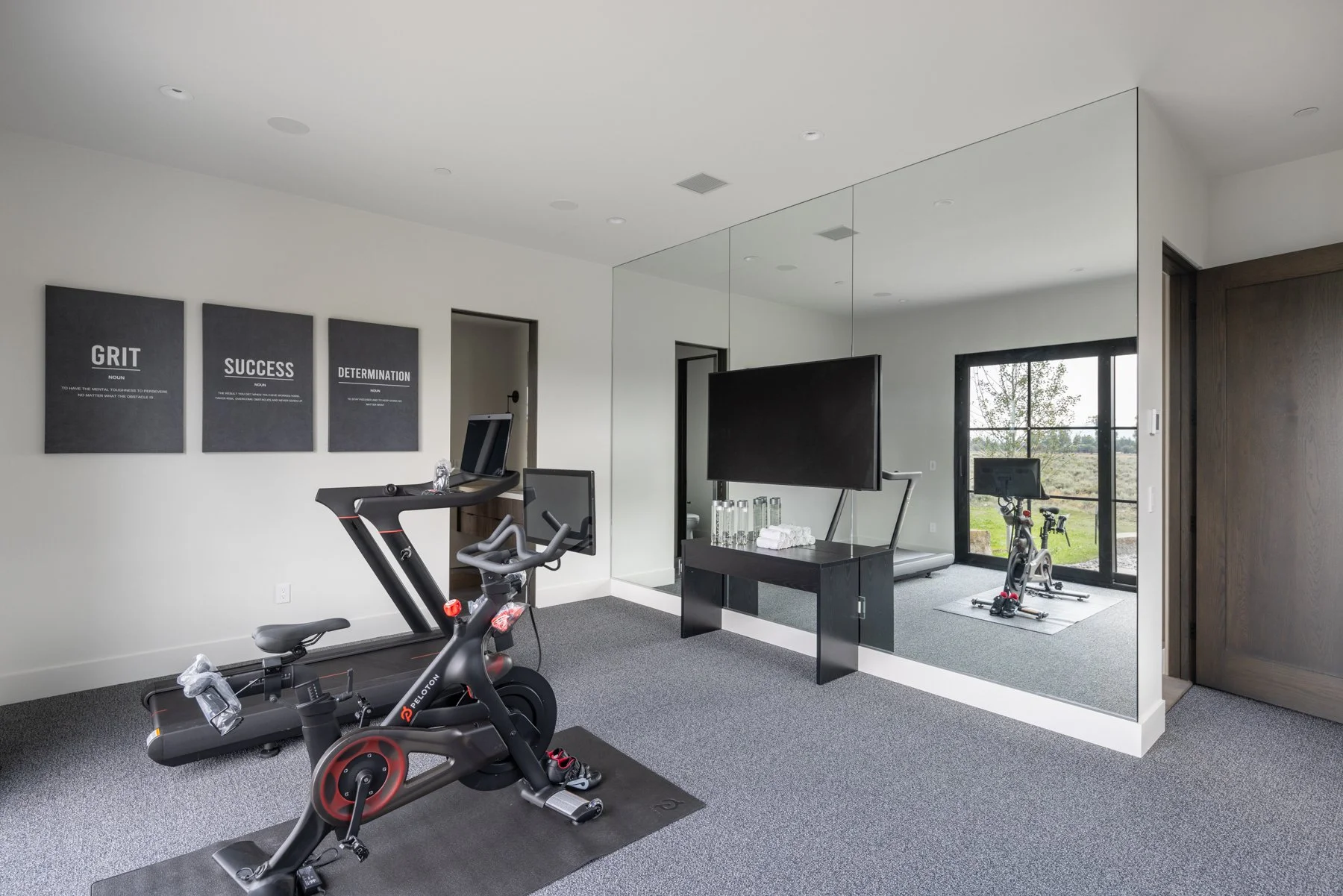 Home gym with exercise bike, treadmill, large TV, motivational wall art, and a mirrored wall.