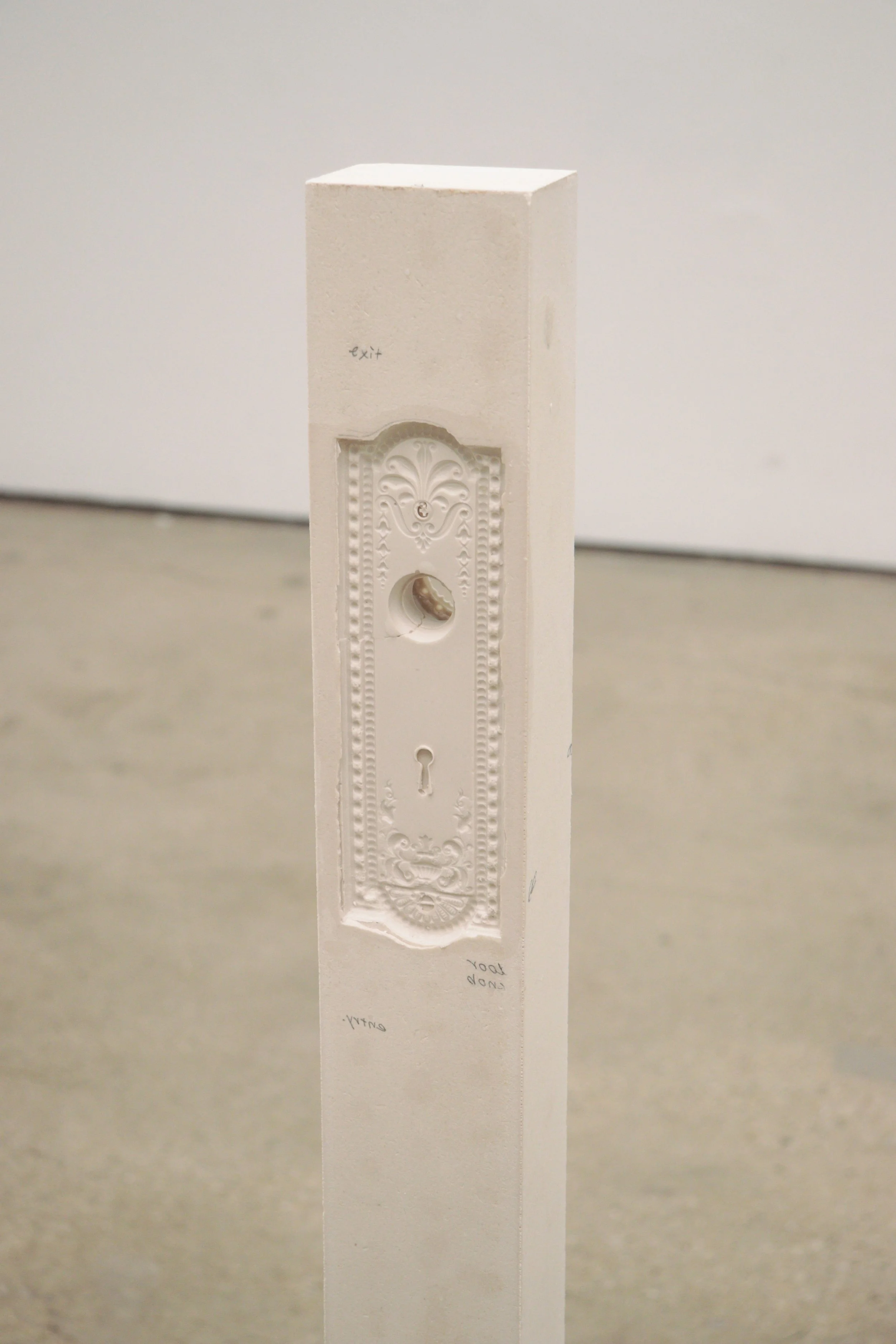 A white, rectangular, decorative wall plate with intricate designs and a keyhole at the bottom.