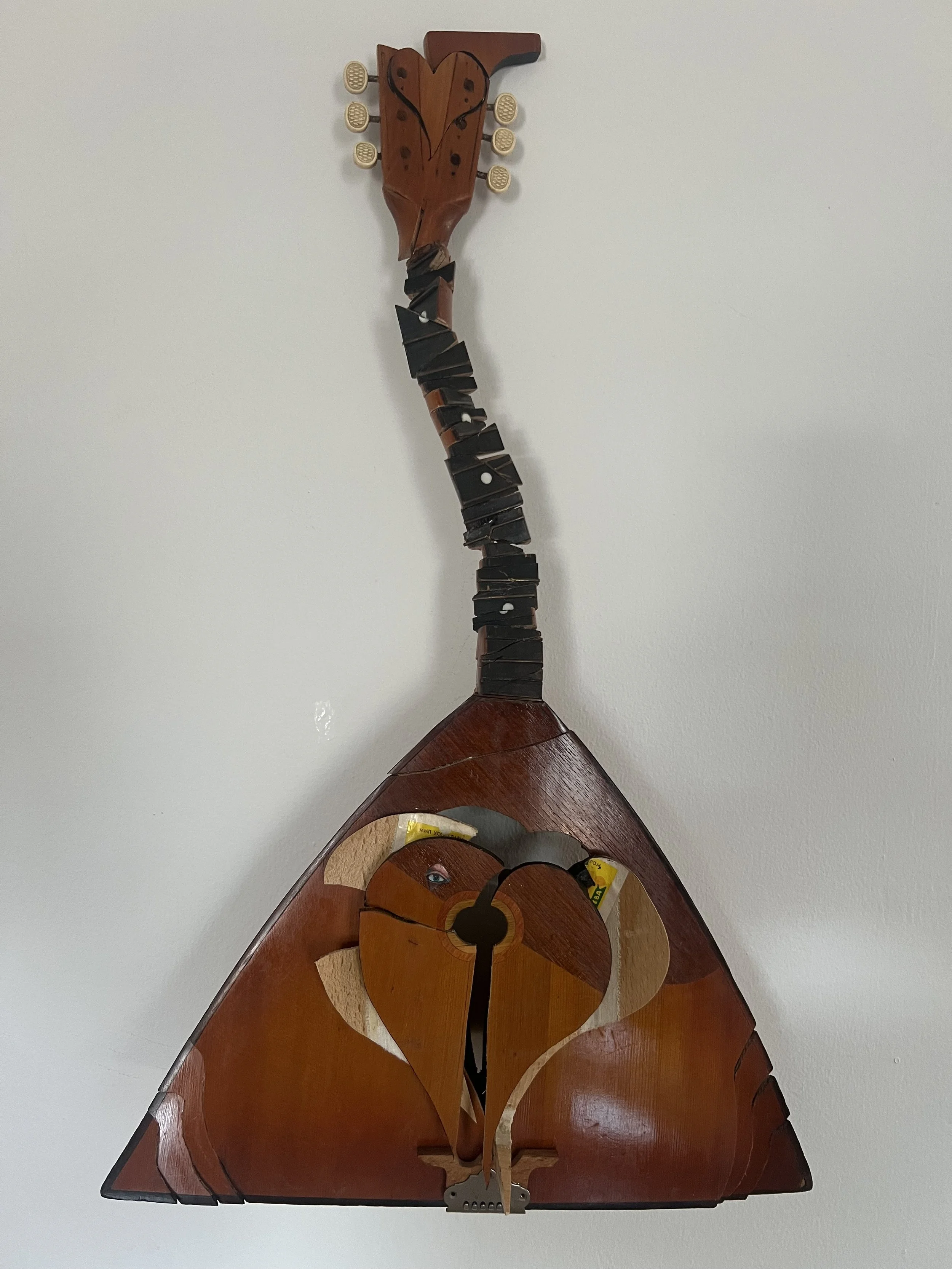 A wooden wall decoration of a guitar with a heart-shaped design on the headstock, set against a plain white wall.