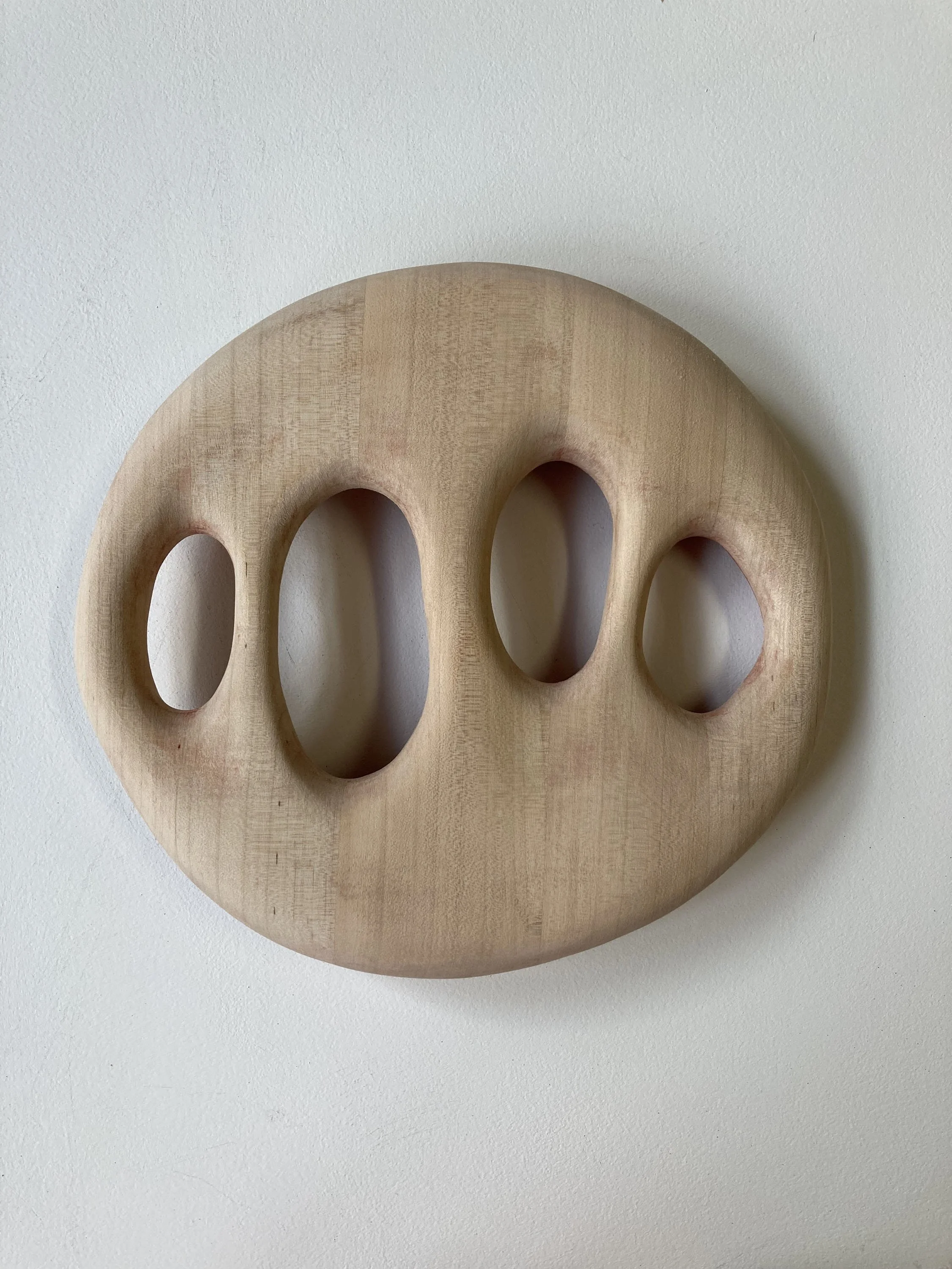 A round wooden object with four oval cutouts, mounted on a white wall.