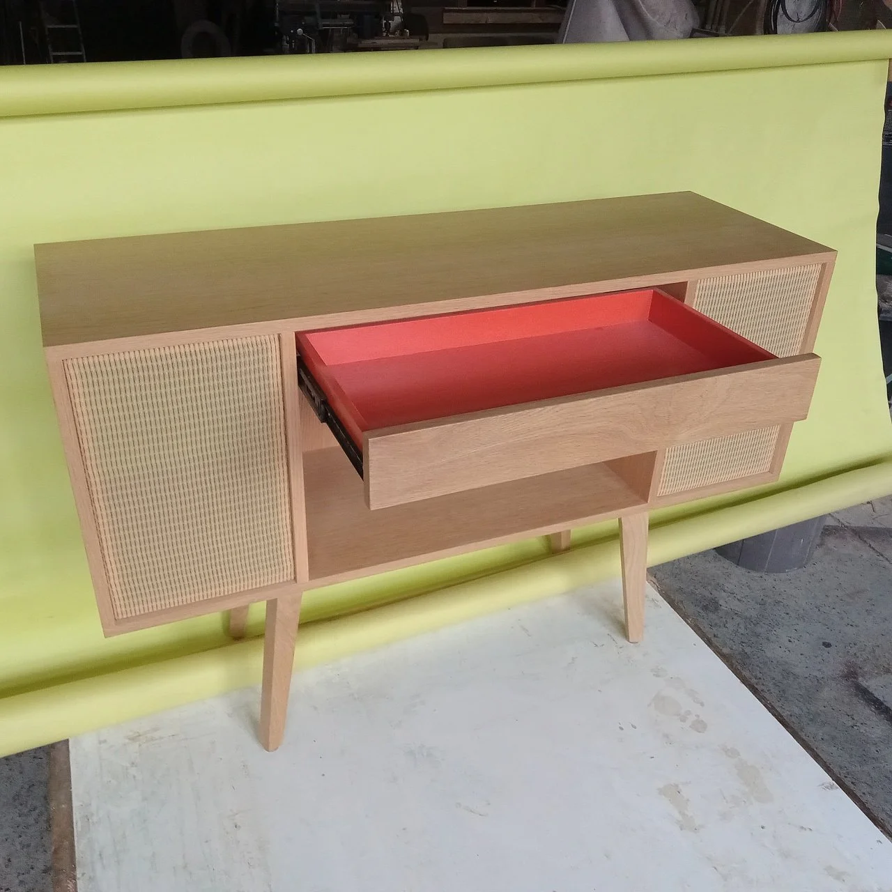 Mid-century modern wooden sideboard with woven cabinet doors and a red tray inside, placed on a yellow surface.