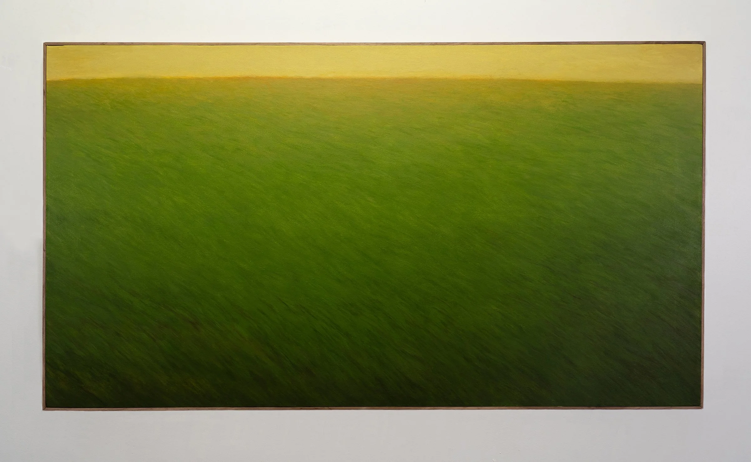 Abstract painting with green and yellow hues framed in wood, hung on a white wall.