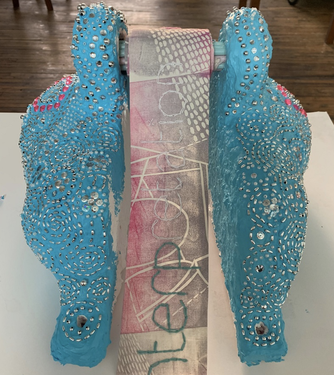 Two large decorative objects with blue paint and silver studs, positioned on either side of a vertical printed banner.