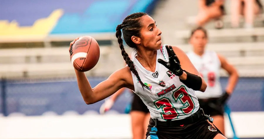 A female football player with braids, wearing a white jersey with number 33, is preparing to throw a football during a game.