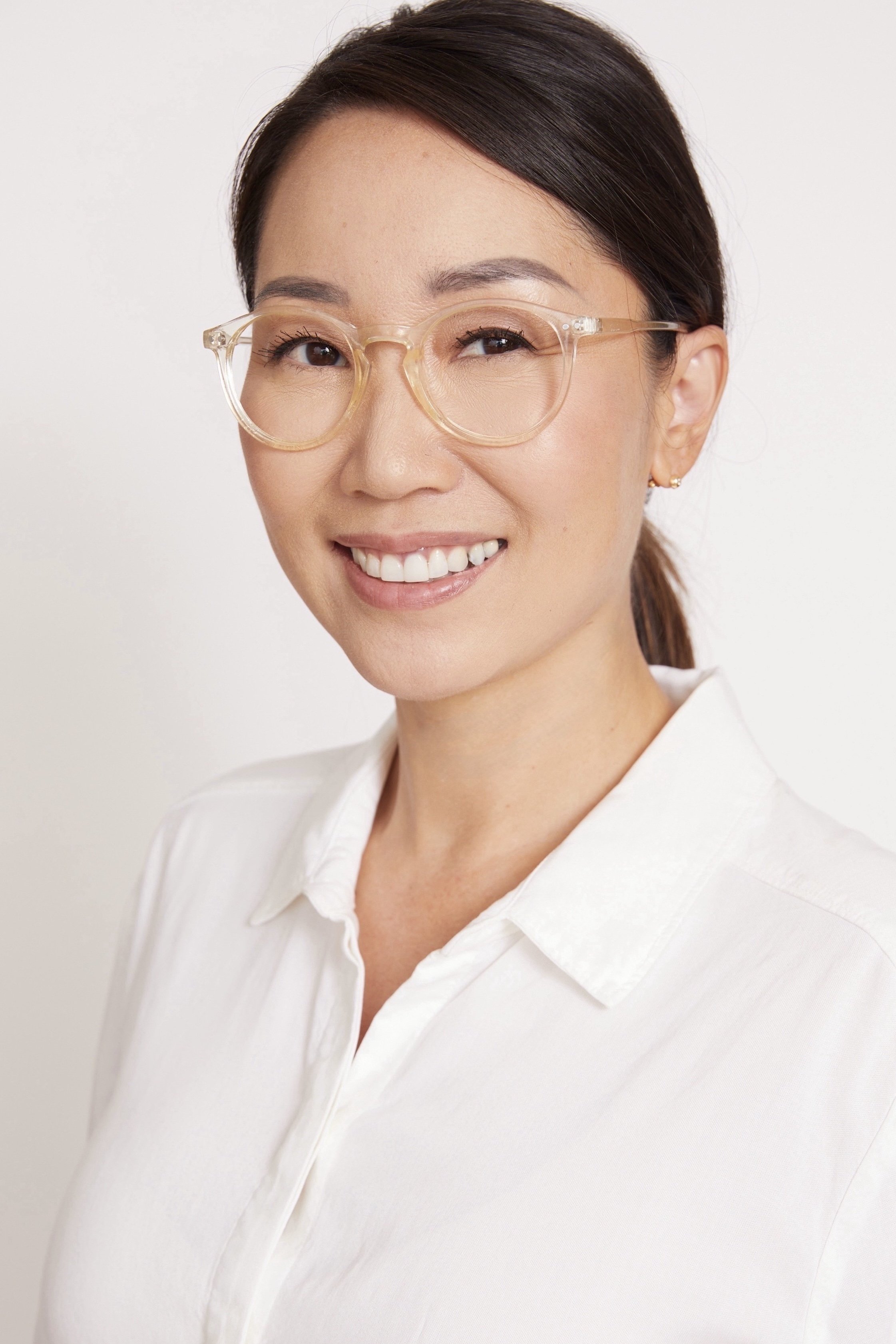 A woman with brown hair, glasses, and a white button-up shirt smiling at the camera against a plain white background.
