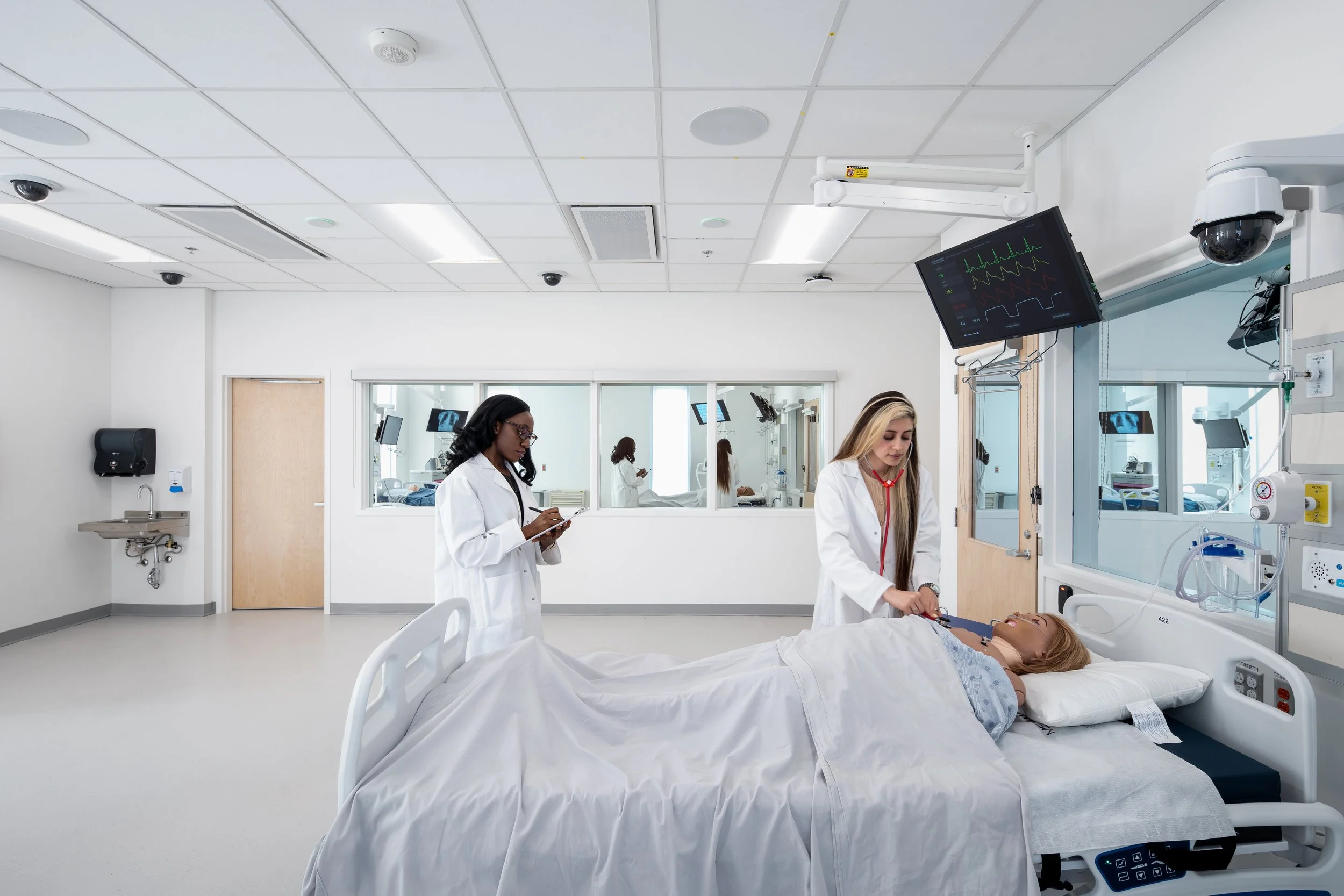 A hospital room with a patient lying in bed while medical professionals attend to her and monitor her vital signs on screens.