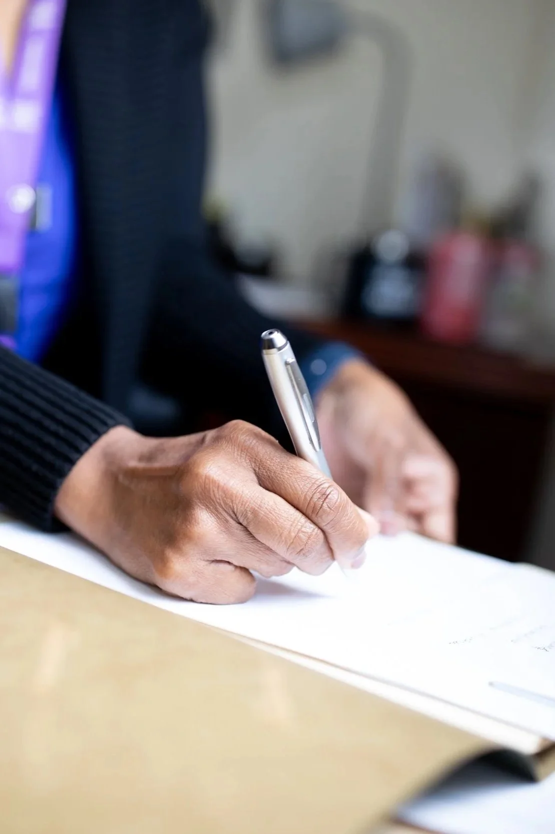 A person writing with a pen on a piece of paper at a desk.