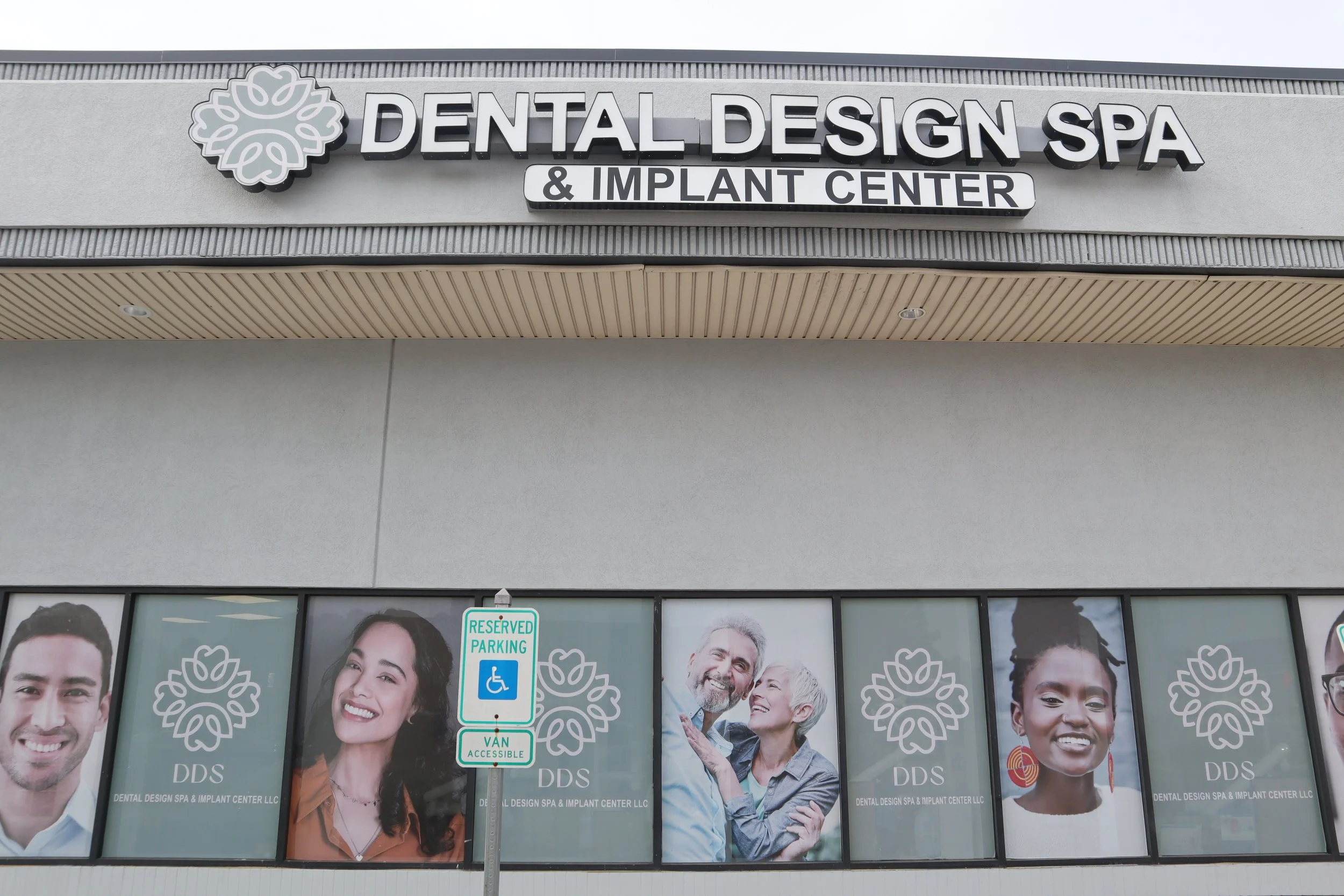 Sign for Dental Design Spa & Implant Center on building exterior, large photographs of diverse smiling people in window display, reserved parking sign in foreground.