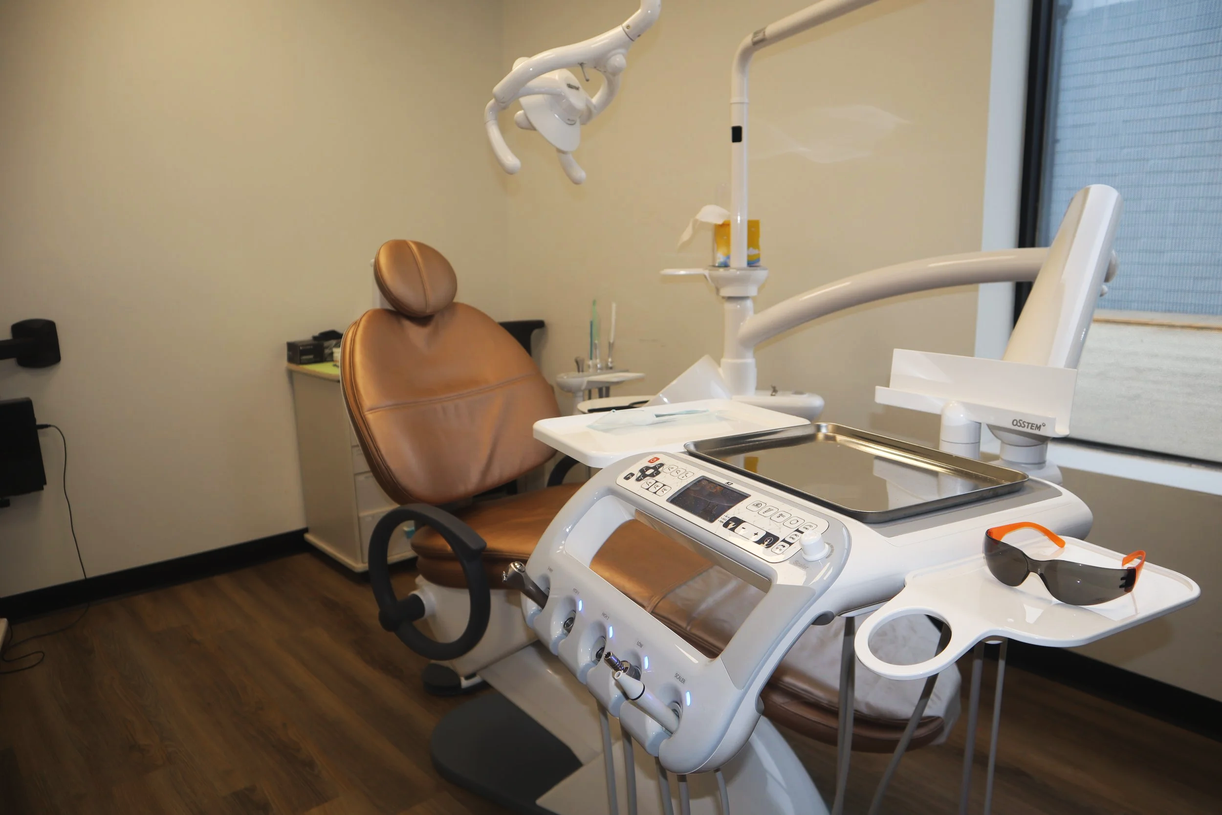 Dental examination room with dental chair, overhead light, sunglasses, and dental tools.