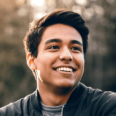 A young man smiling outdoors with sunlight in the background.