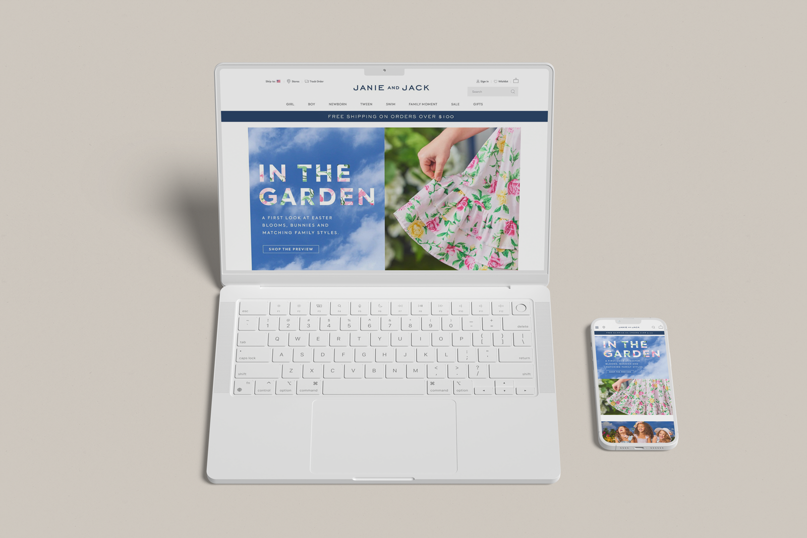 Open white laptop and white smartphone displaying a website called Janie and Jack with a garden-themed Easter collection shown on the screens, placed on a beige surface.