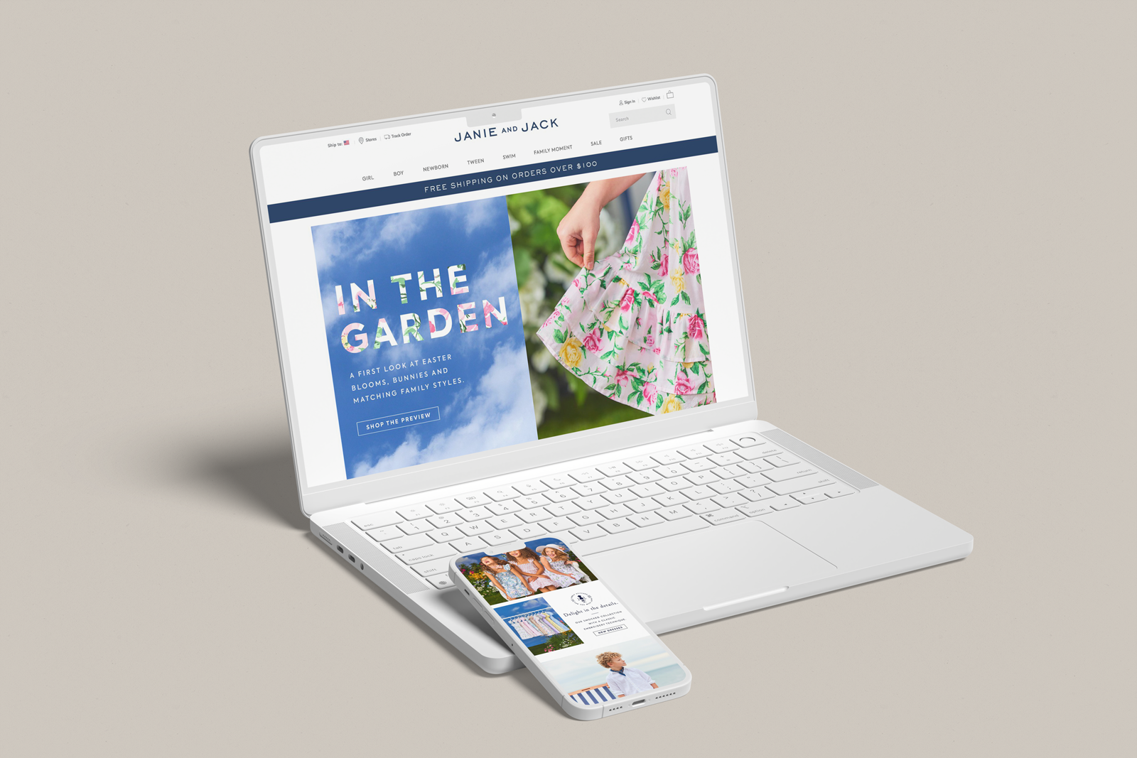 A white laptop displaying an online shopping website for children's clothing, with a phone showing additional clothing items, all on a beige surface.