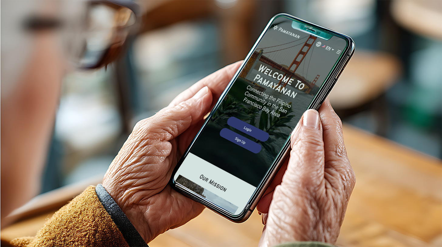 A person holding a smartphone displaying the welcome page for the community app 'Pamayanan,' with an image of the Golden Gate Bridge and text about connecting the Filipino community in the San Francisco Bay Area.