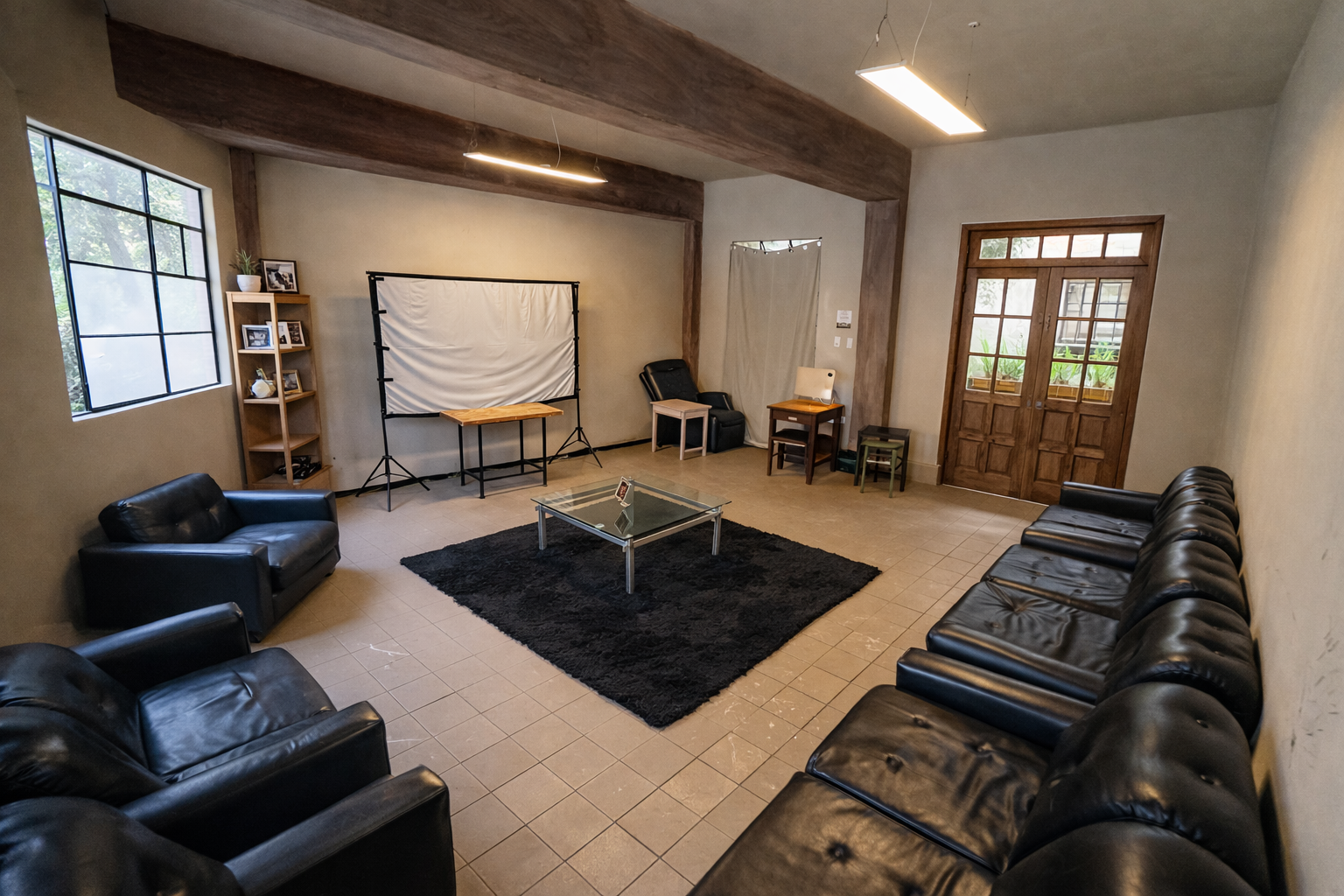 Sala de estar con sillones de cuero negro, mesa de cristal, alfombra negra, con equipo de fotografía y ventanas de madera.