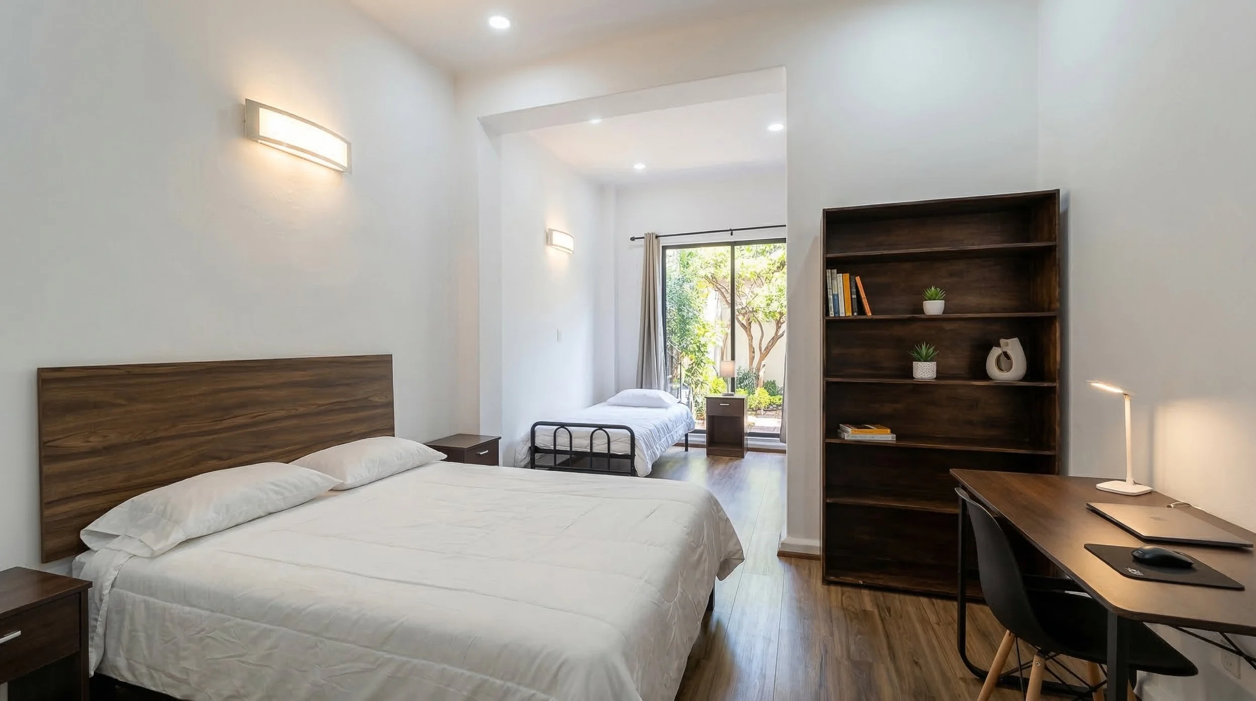 Habitación moderna con cama grande, cama individual, estantería de madera, escritorio con lámpara y computadora, ventanales con vista a un jardín.