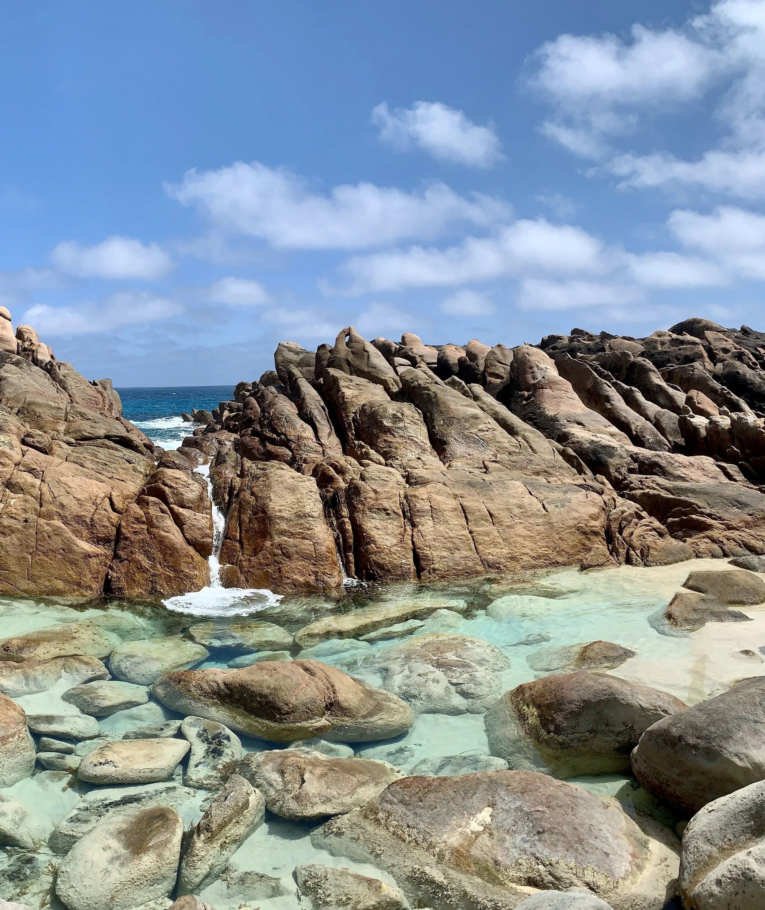 A rocky beach with clear water, large rocks, and a partly cloudy sky.