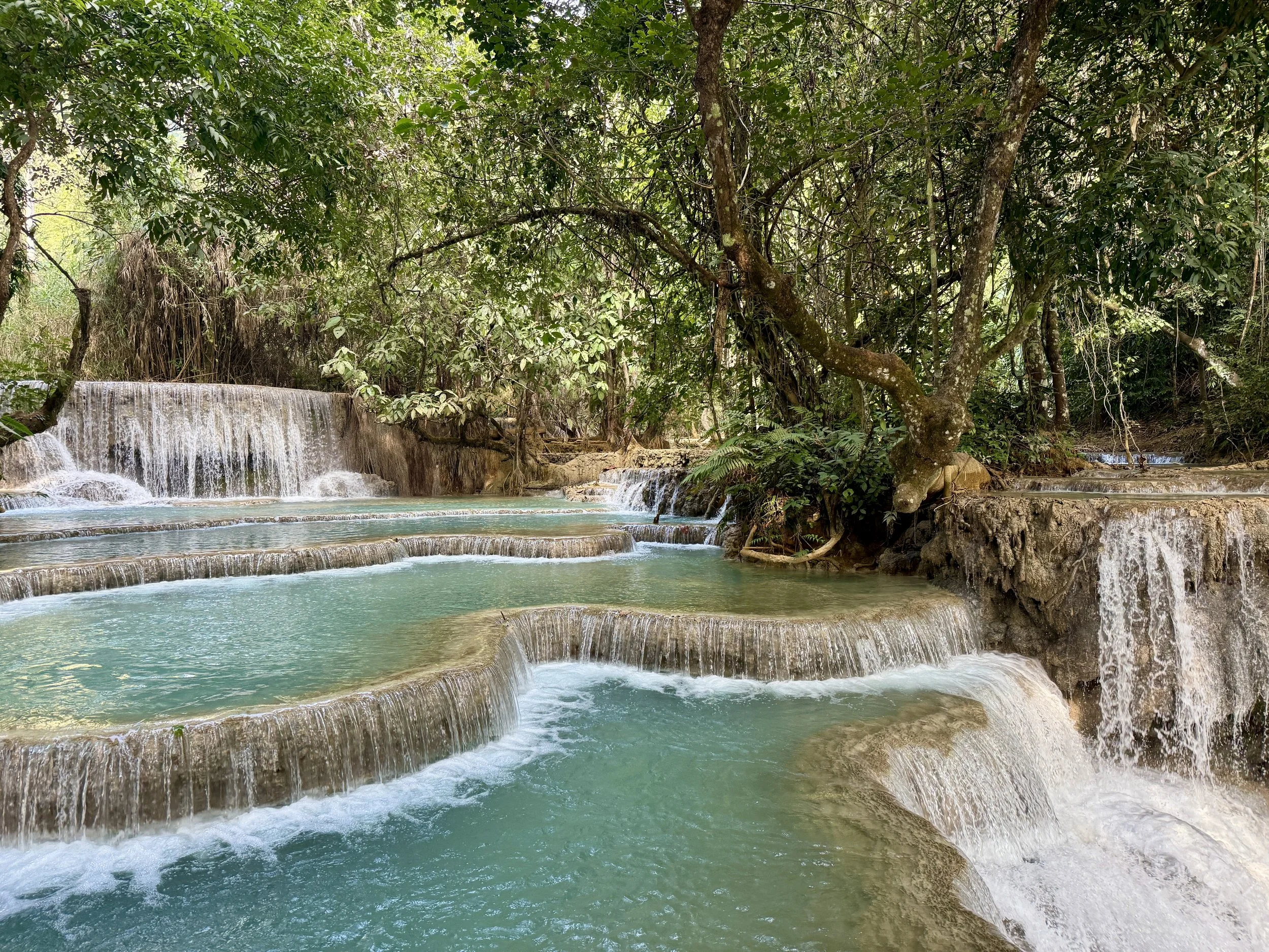 Flowing tiers of a natural turquoise waterfall in a lush green tropical forest.