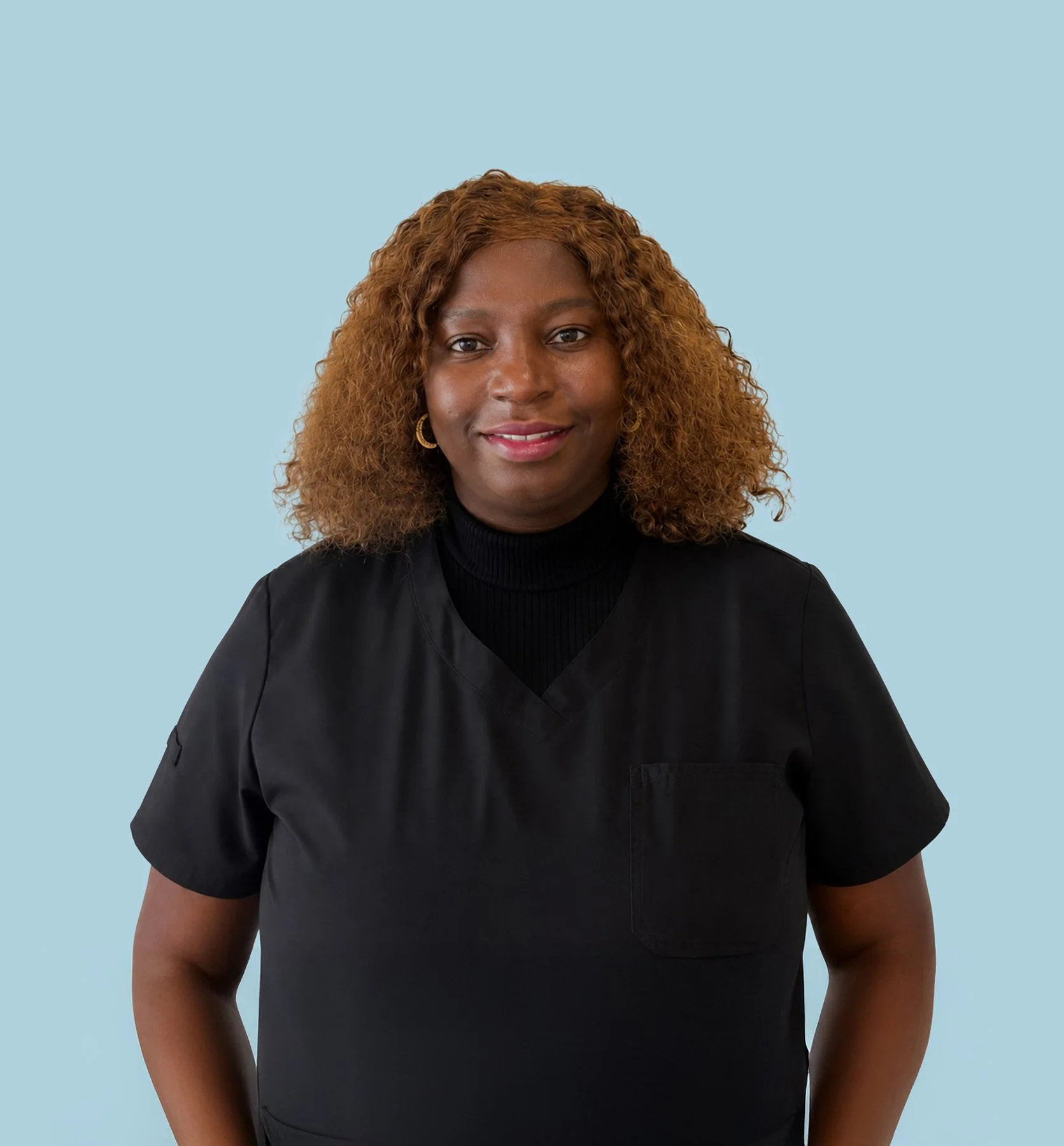 A woman with dark skin, curly light brown hair, wearing a black top, standing against a light blue background.