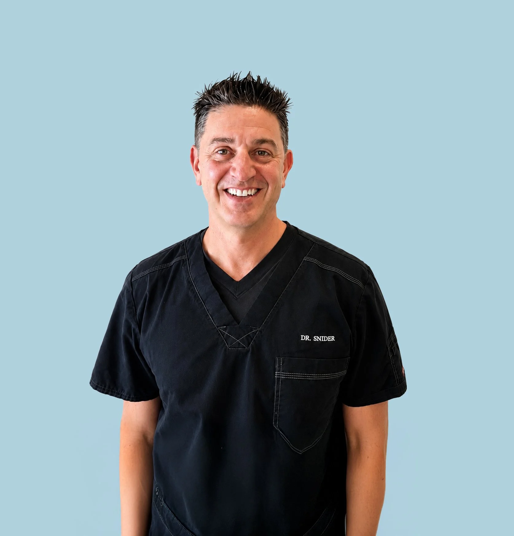 A smiling man wearing black medical scrubs with "DR. SNIDER" embroidered on it, standing against a light blue background.