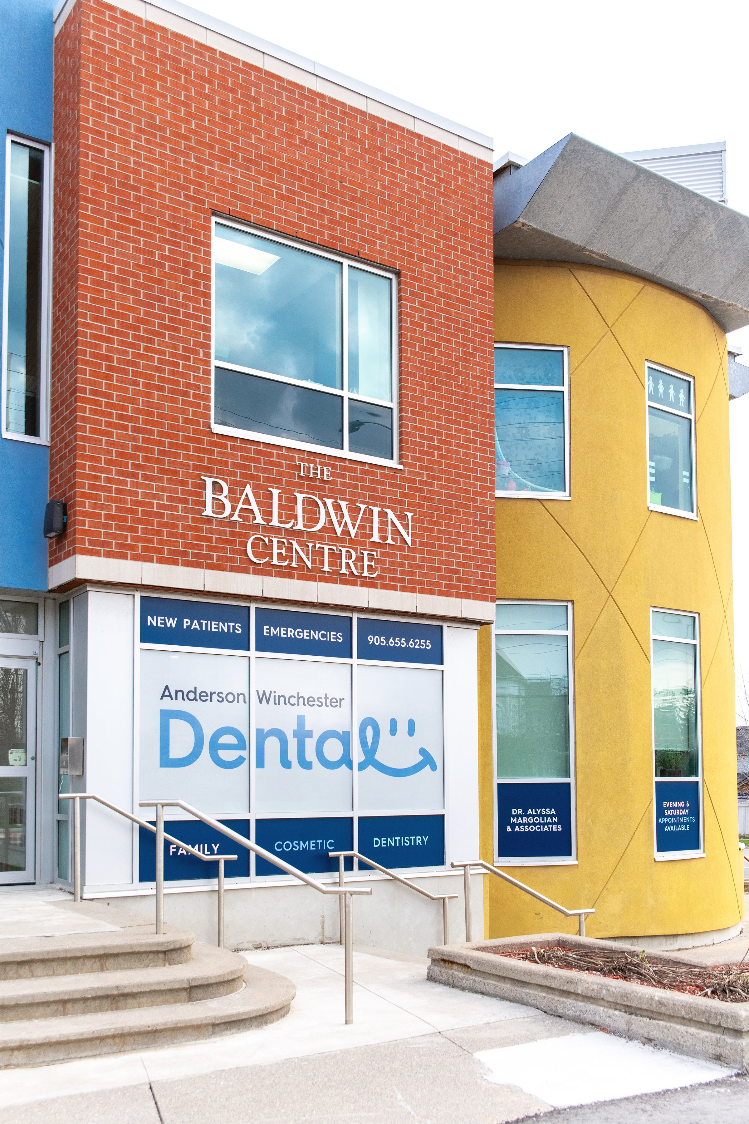 Exterior view of a dental clinic named Anderson Winchester Dental, showing colorful building with red brick, yellow, and blue walls. Signage indicates dental services and appointments.