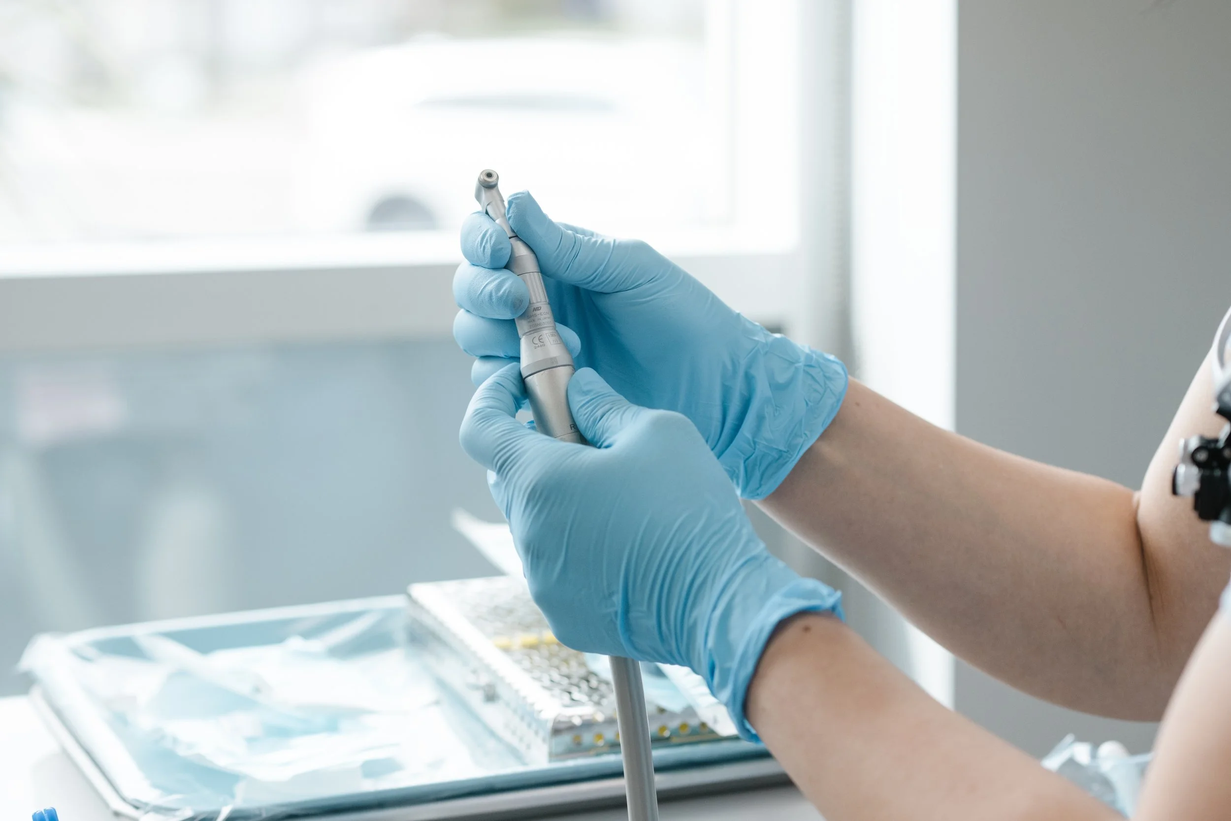 A healthcare worker wearing blue gloves holding a dental drill or similar medical instrument.
