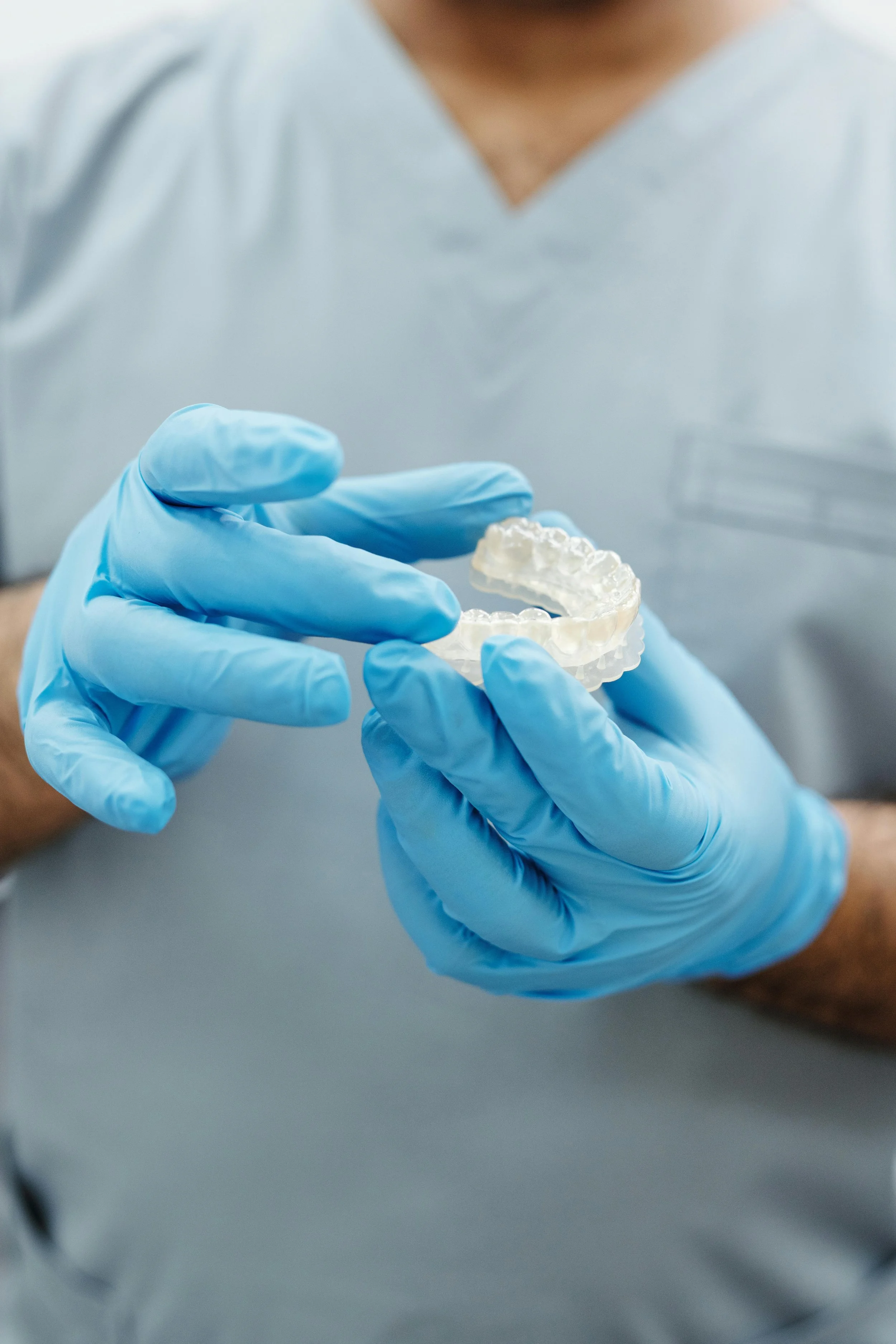 Person wearing blue gloves holding a clear dental or medical mold.