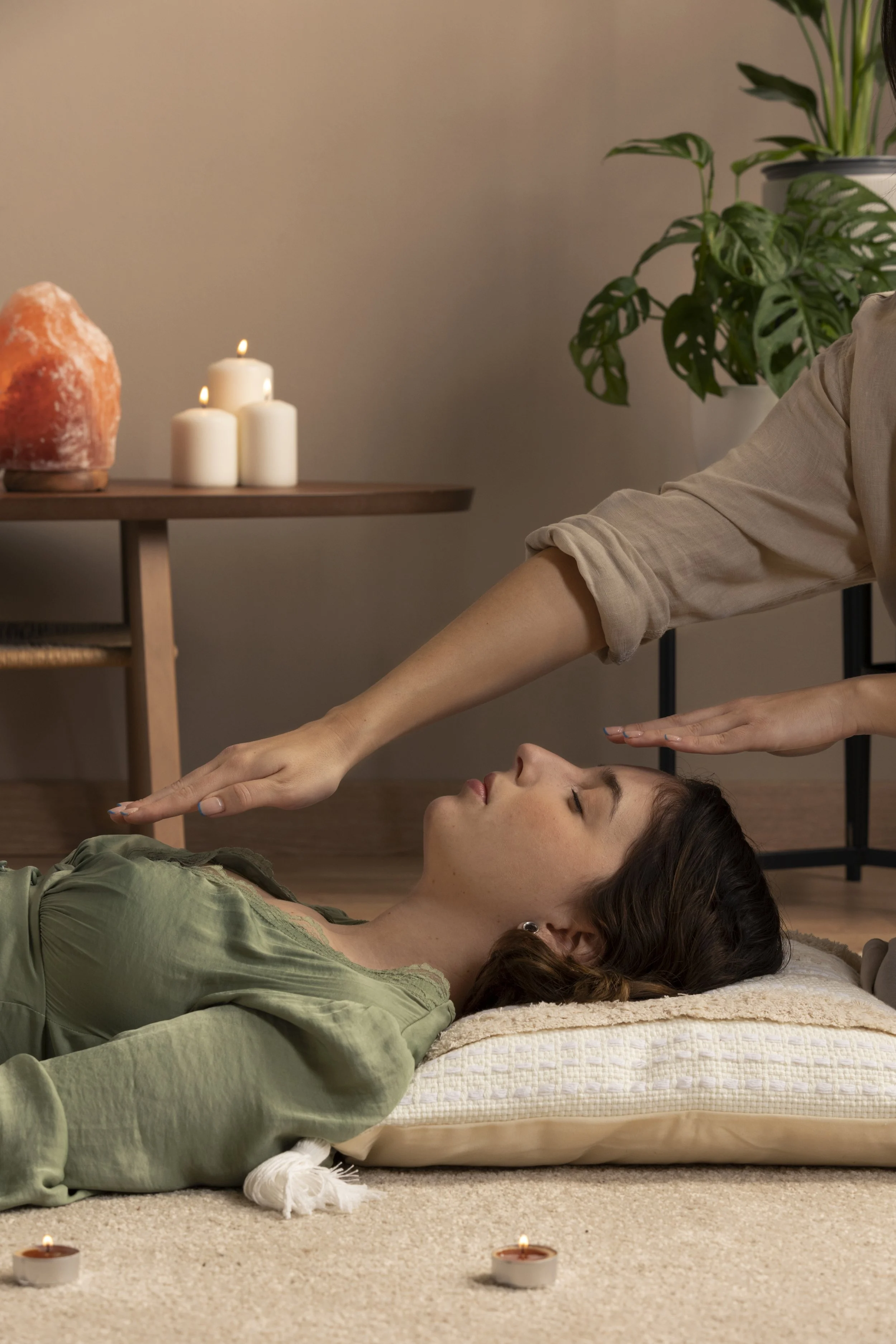 A woman receiving a relaxation or healing session with candles and plants in the background.