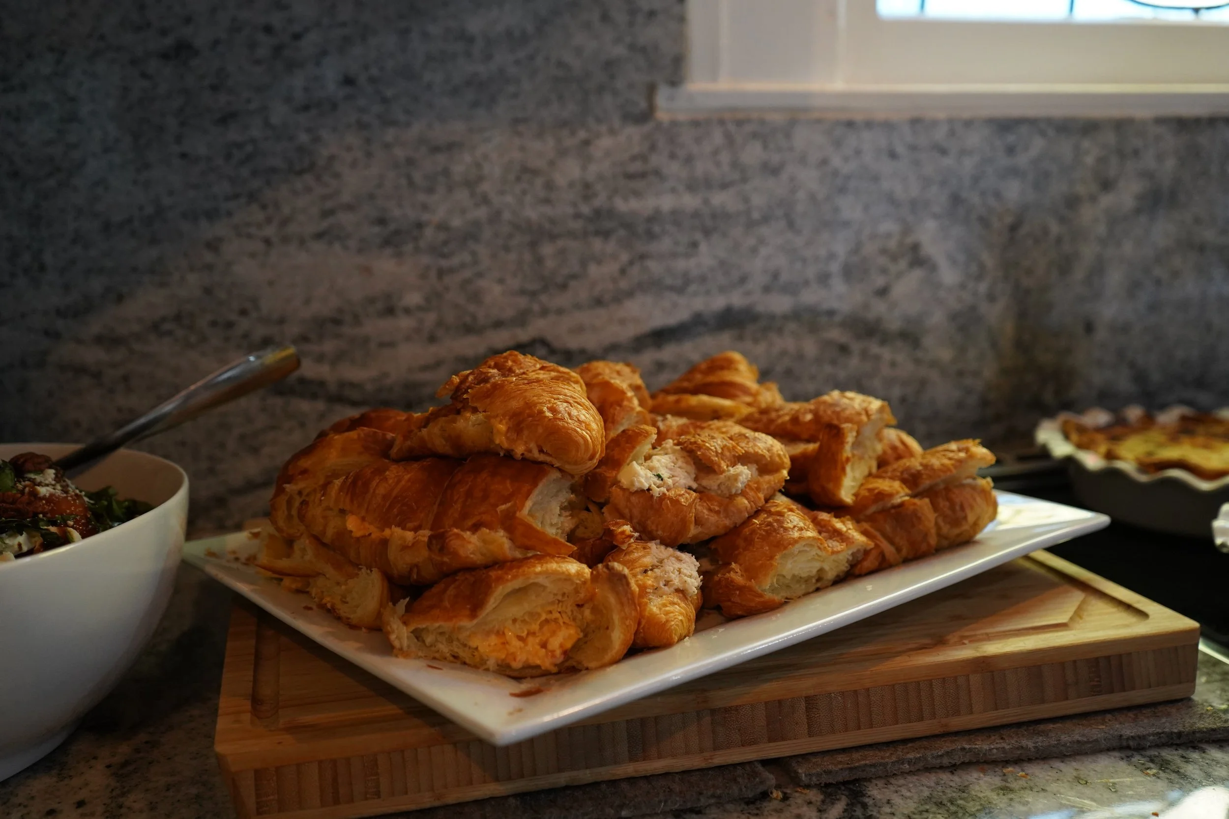 A plate of sliced croissants on a wooden board in a kitchen counter setting.