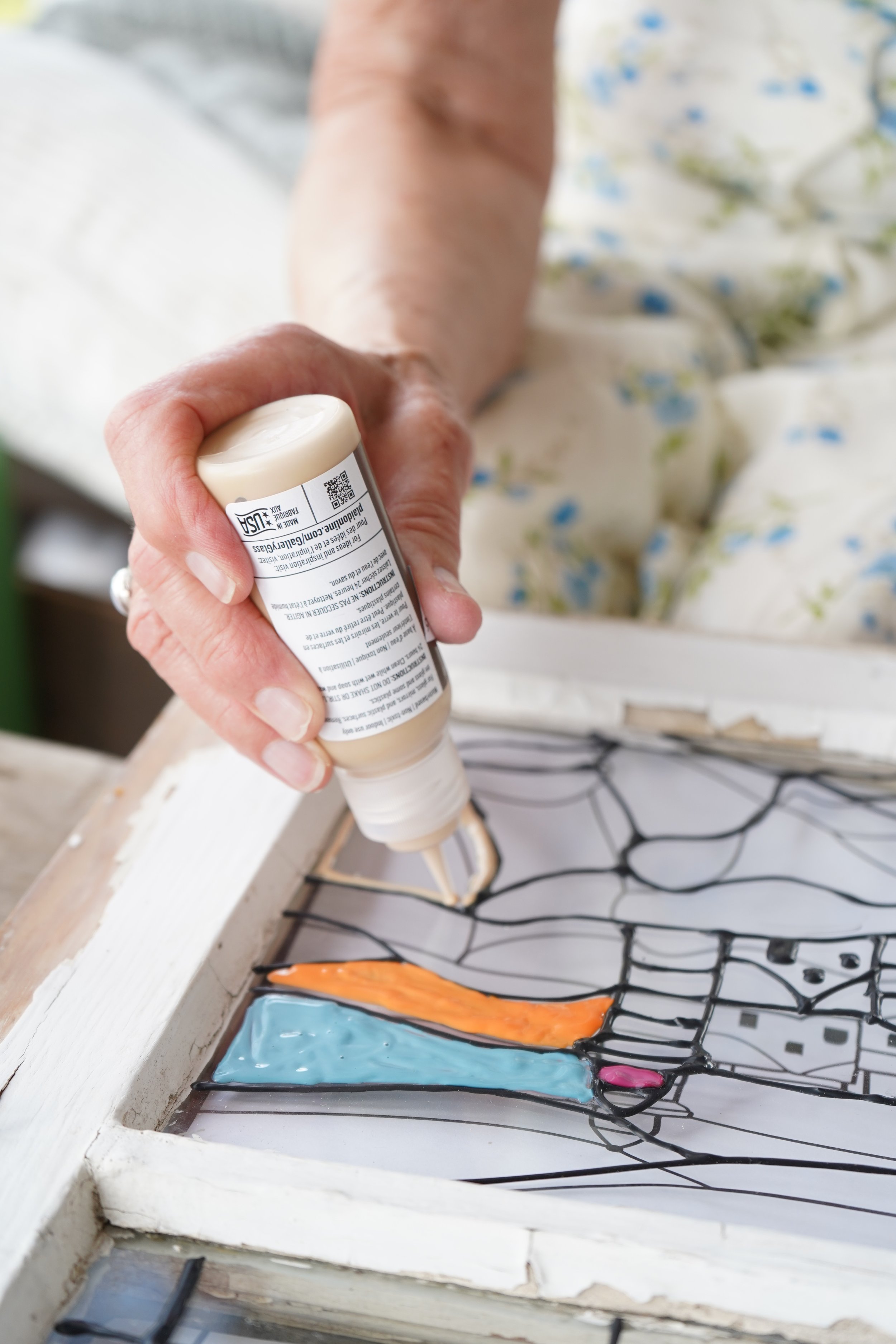 Person applying glue on a stained glass artwork that depicts a unicorn, with a colorful mane and face, in a wooden frame.