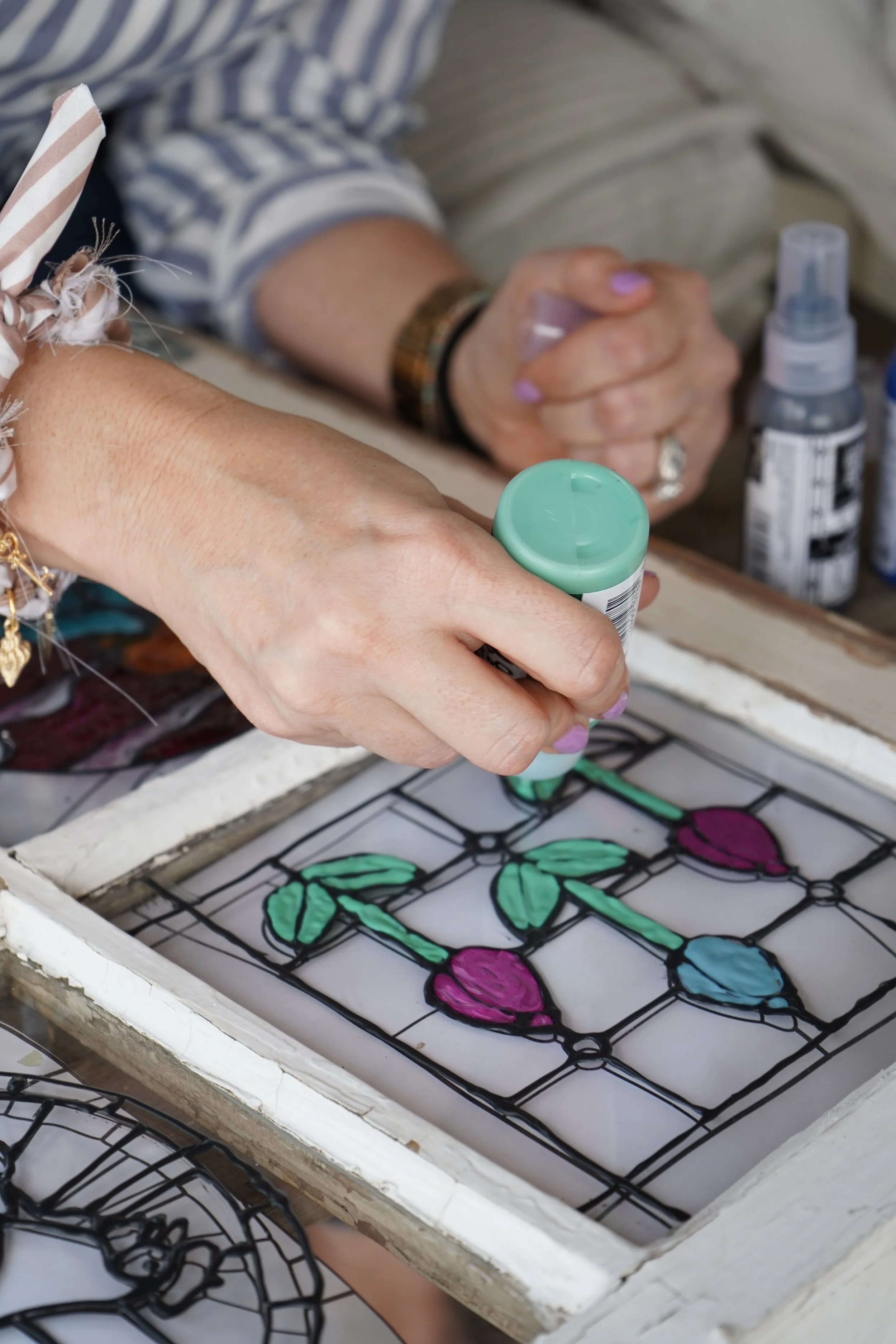 Person using a green marker to color stained glass window with pink and blue flowers and green leaves.