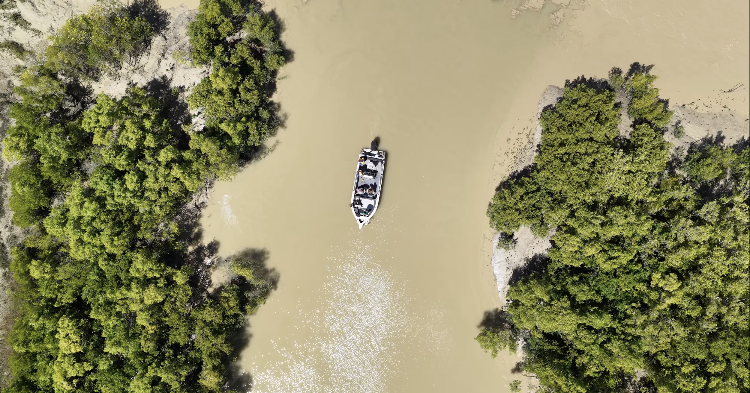 Drone aerial view of a fishing boat navigating muddy mangrove channels in the wild waterways surrounding Darwin, Australia.