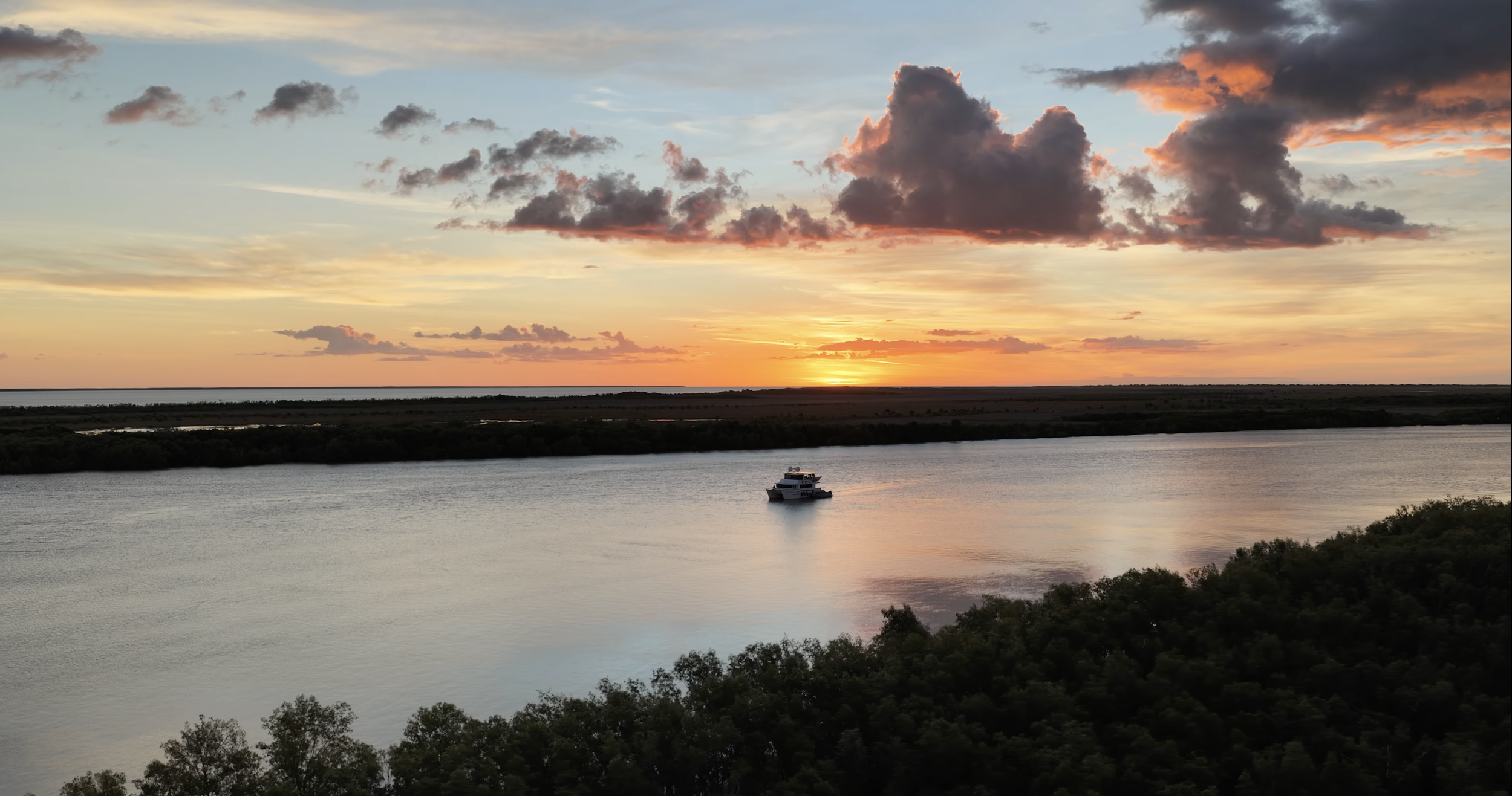 Drone cinematography of a yacht cruising through the remote waterways of Darwin at sunset, surrounded by mangroves and dramatic Northern Territory skies.