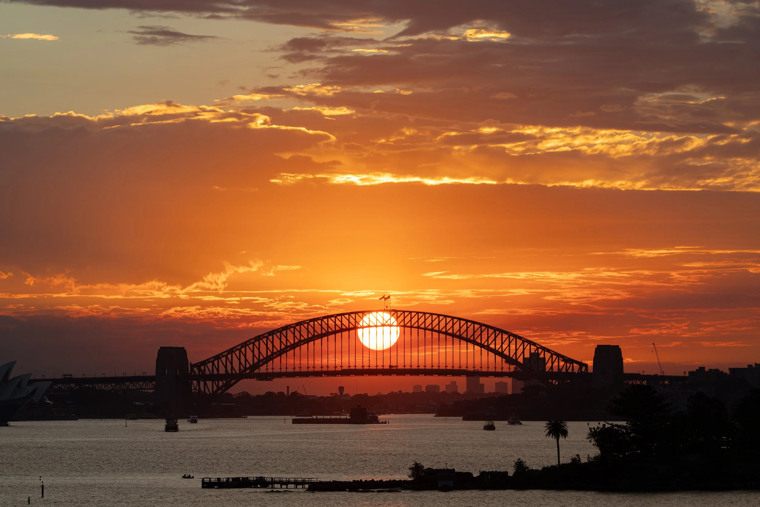 Sunset behind Sydney Harbour Bridge with the sun aligned under the bridge