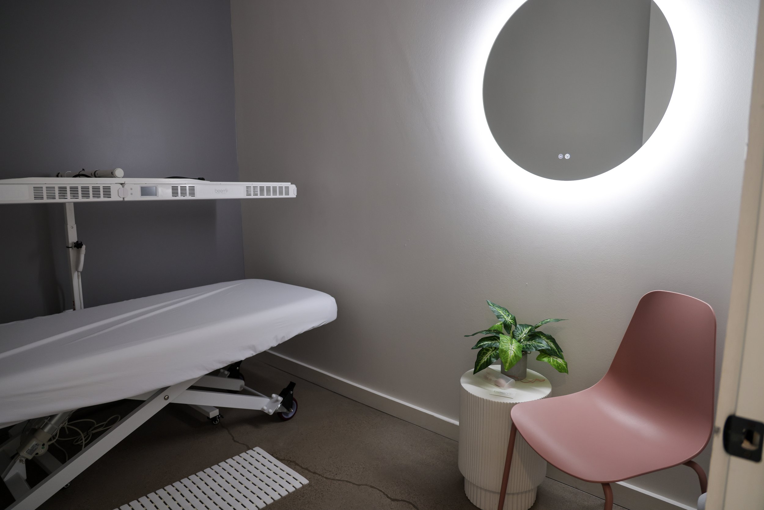A Private red light room with a pink chair, a bed, and a red light panel.