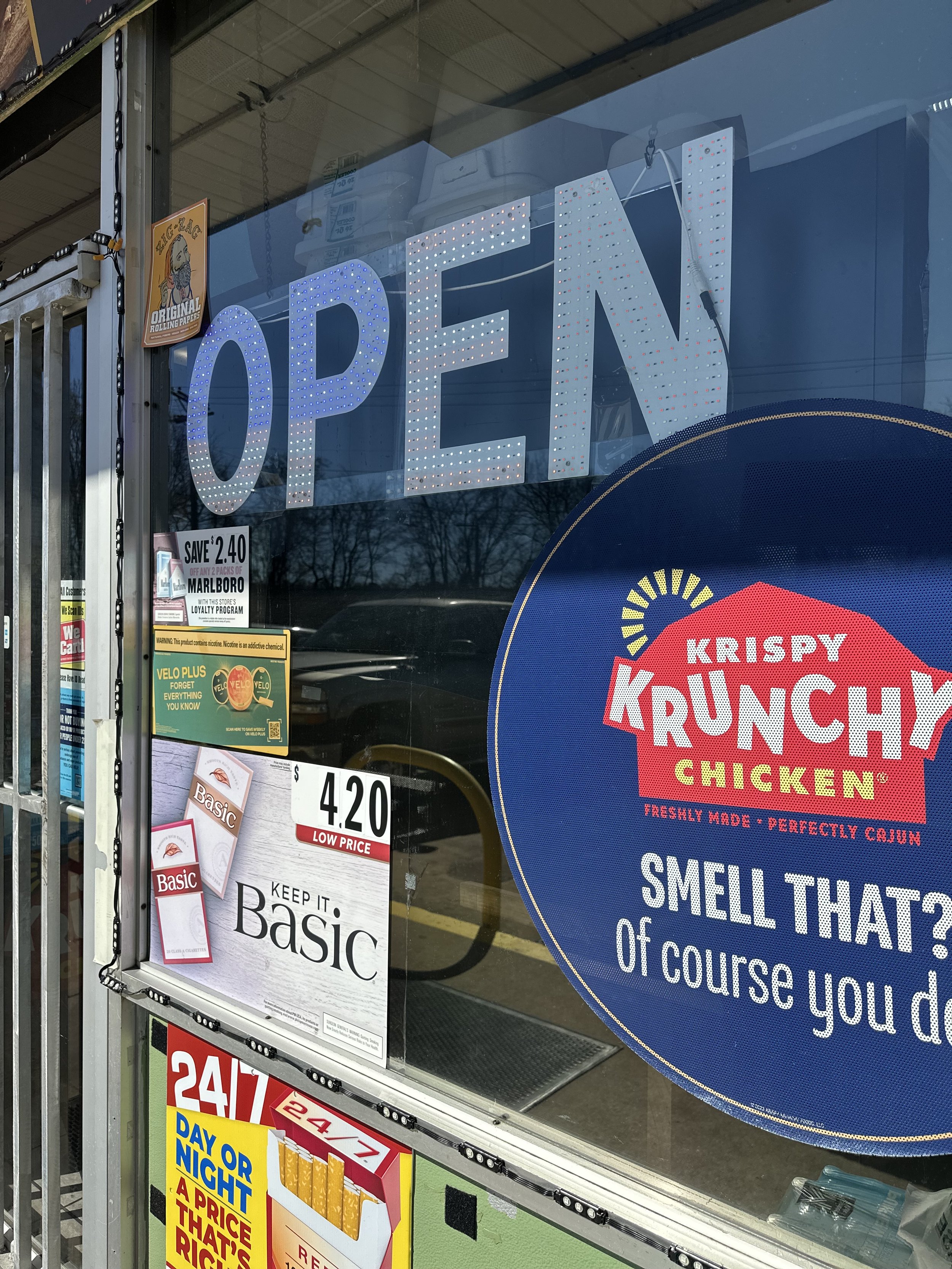 Open Signs & Featured Deals adorn the front doors of Nisha One Stop + ENJ. Customers can enjoy sodas, slushies, chicken and more daily essentials at affordable rates.
