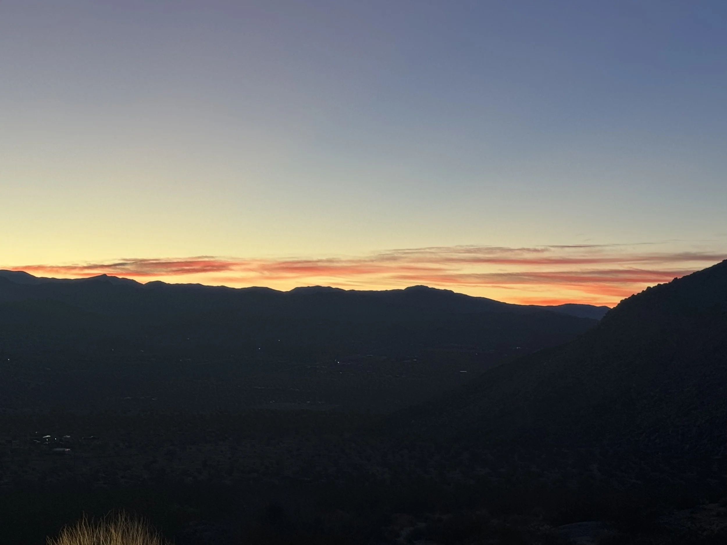 Sunset over mountain range with dark silhouettes of hills and a colorful sky.