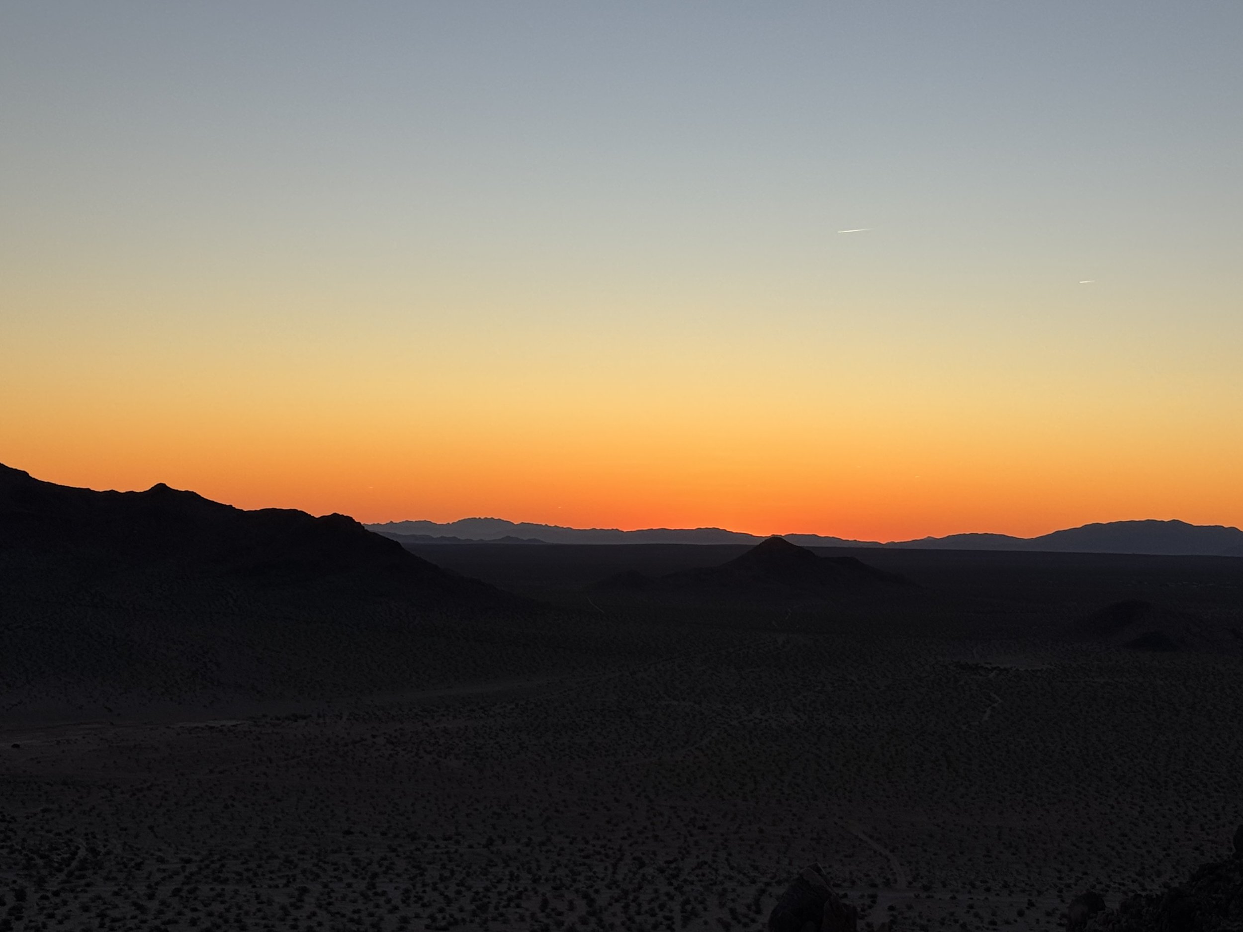 Sunset over desert mountains with a vibrant orange and blue sky.