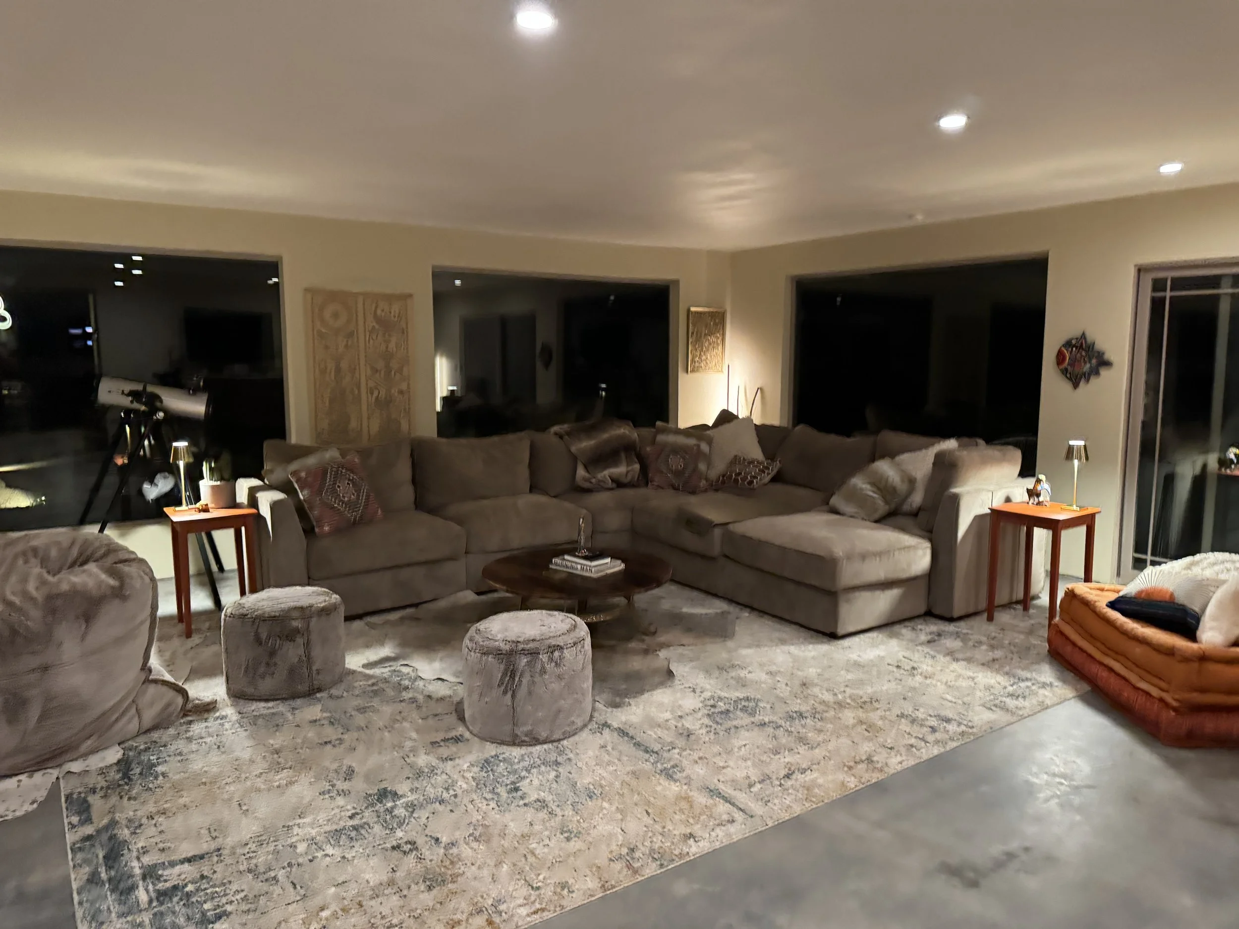 Living room with large sectional sofa, two side tables with lamps, a telescope near the window, and an area rug.