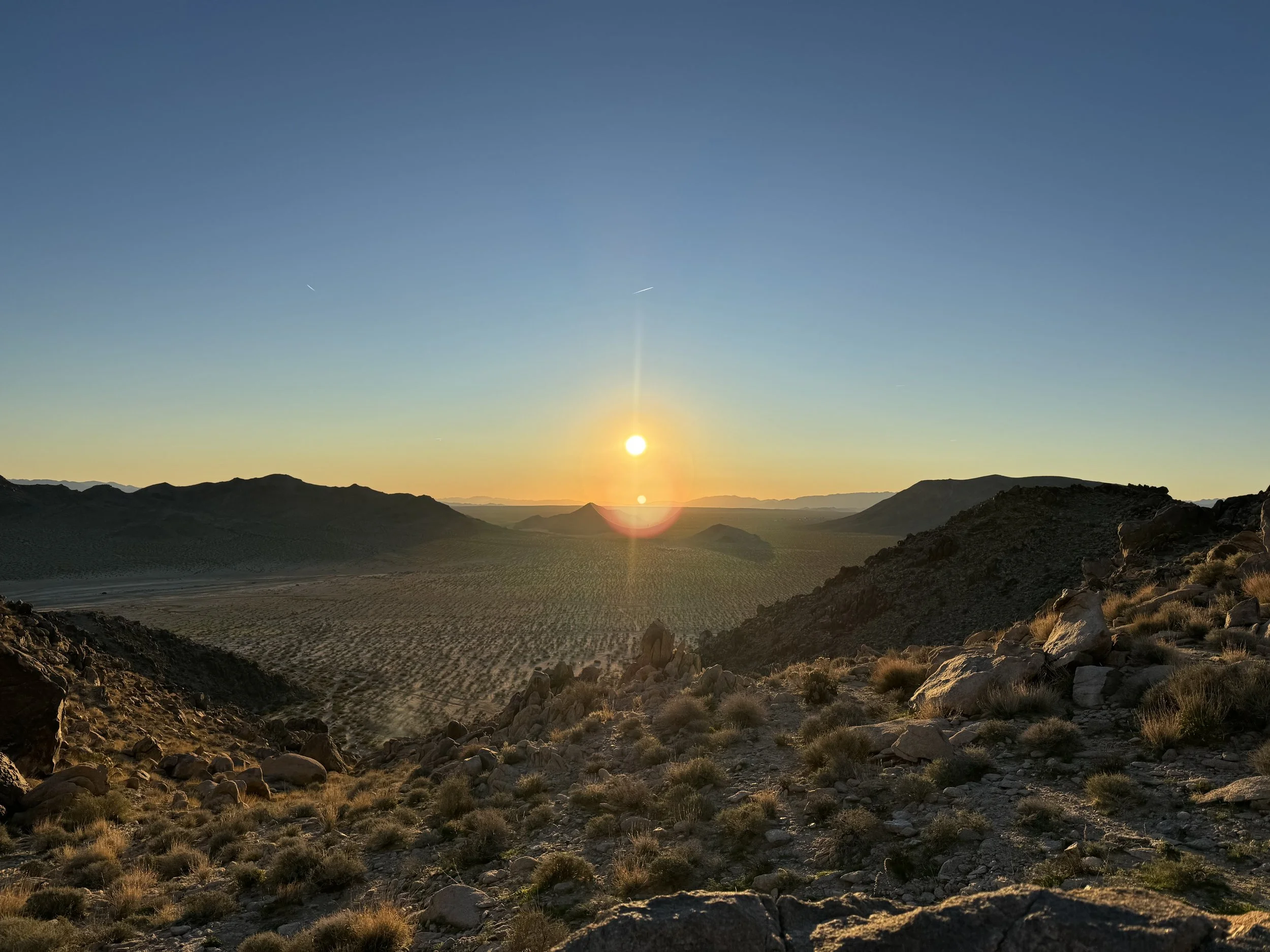 Sunset over a desert landscape with rocky hills and sparse vegetation.