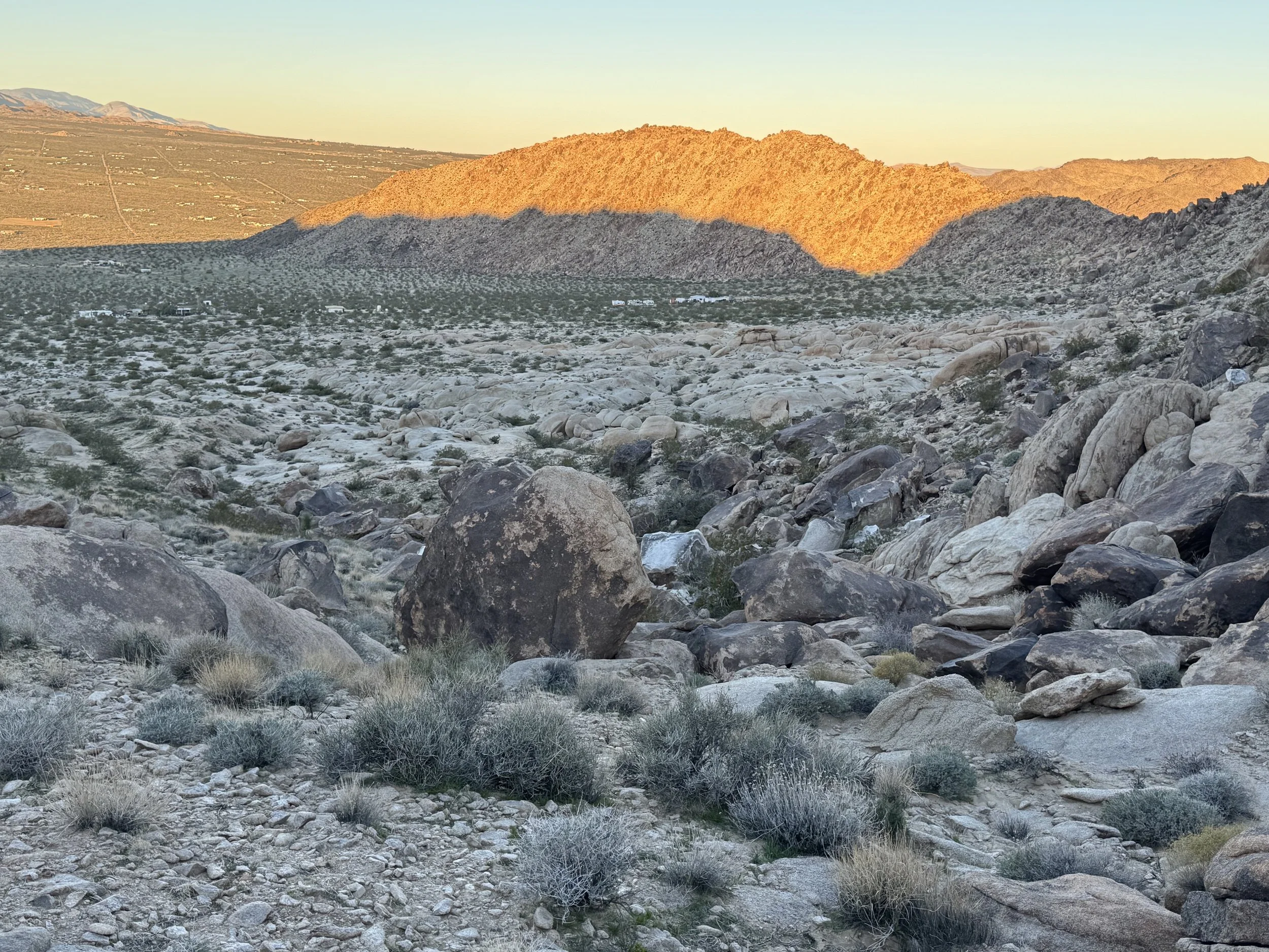 A desert landscape with large rocks and sparse sagebrush in the foreground, mountains in the background, and a clear sky.