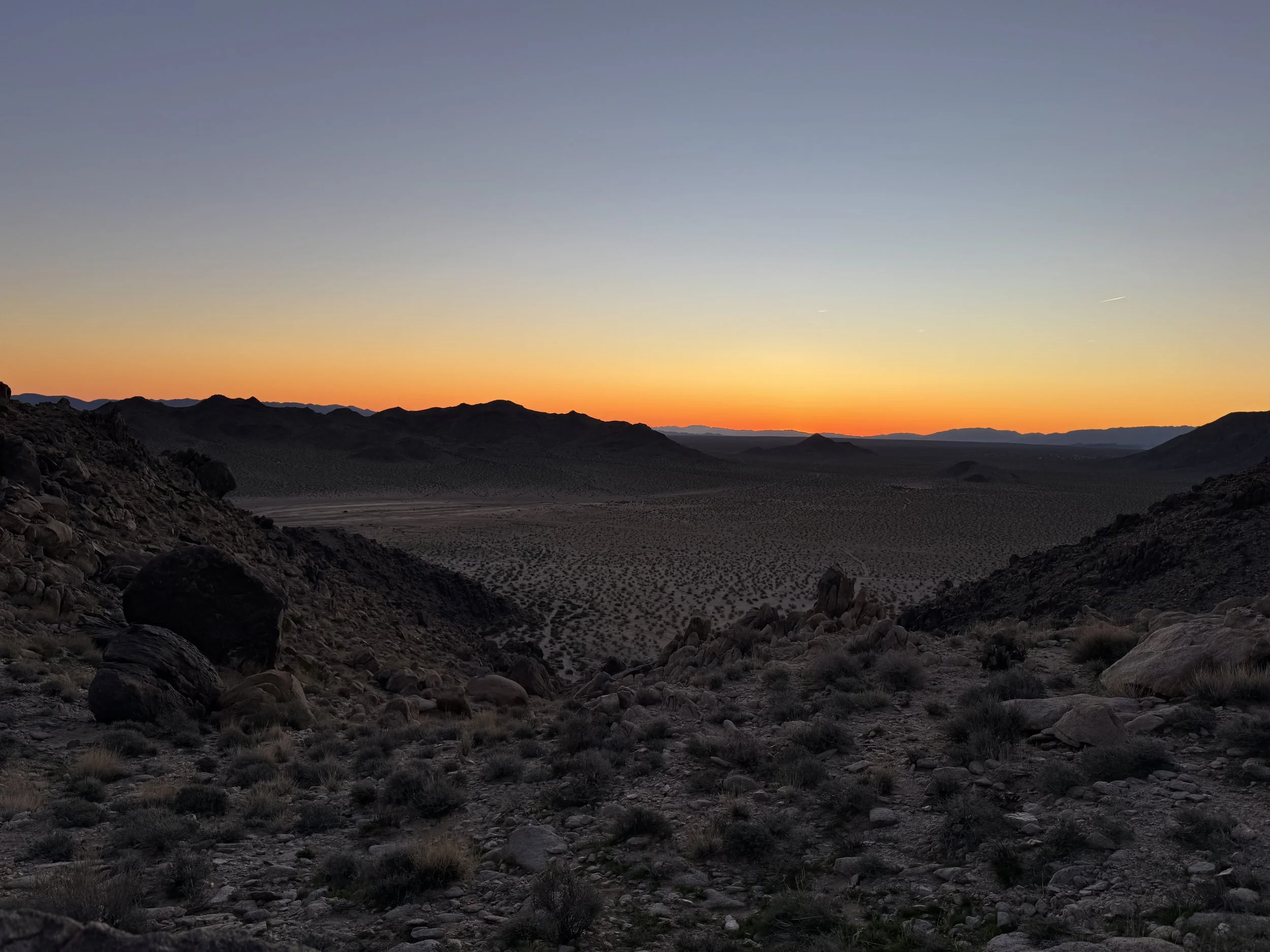 Desert landscape at sunset with rocky hills and sparse vegetation