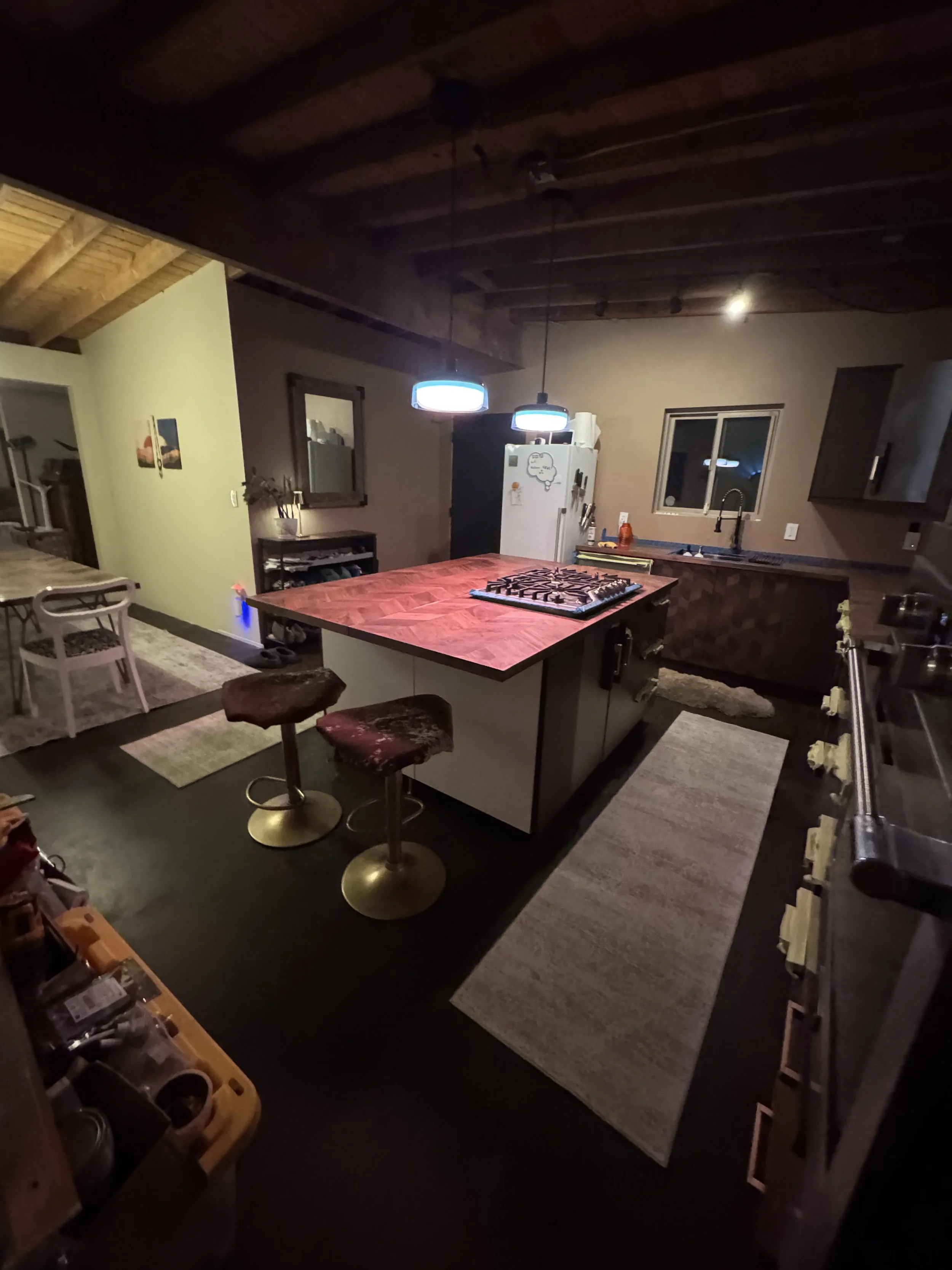 Kitchen with a central island, two bar stools, a white refrigerator, a window over the sink, and wooden ceiling beams.