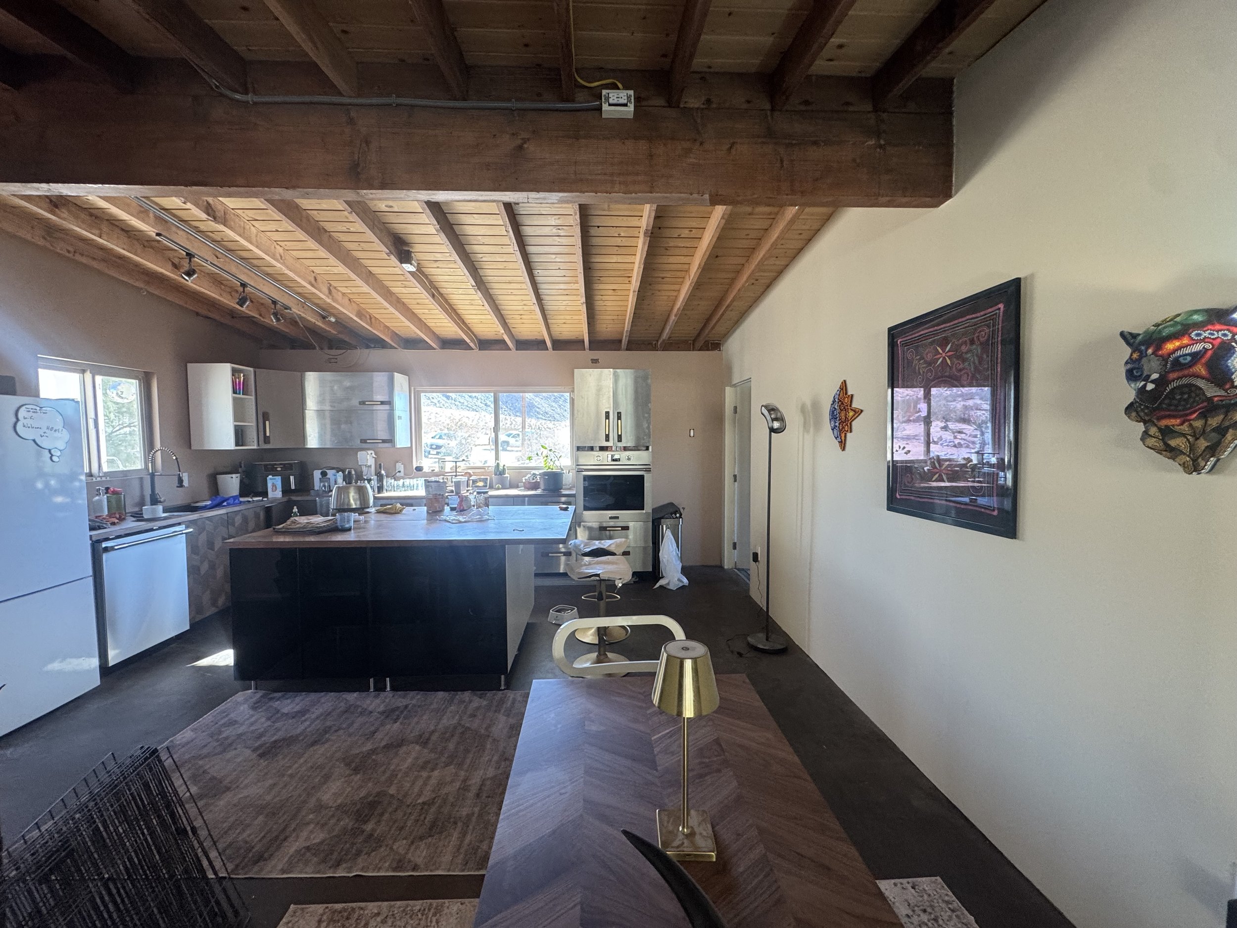 Kitchen with wooden ceiling, white and black cabinets, appliances, dining table with gold lamp, and wall decorations.