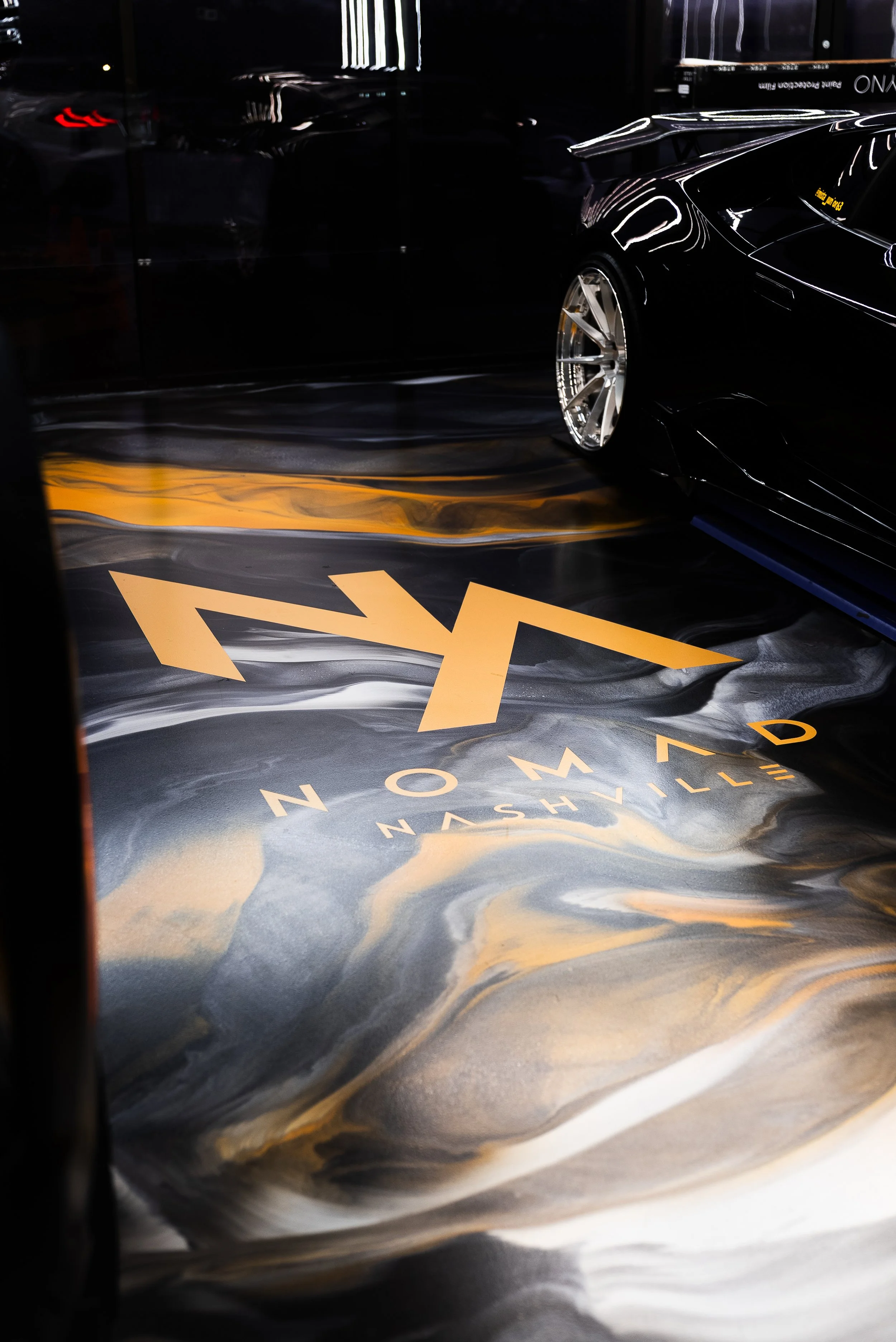 A close-up view of a black luxury car parked on a marble-patterned floor with the words "NASHVILLE" and "N" visible on the floor. Marble look epoxy floors.