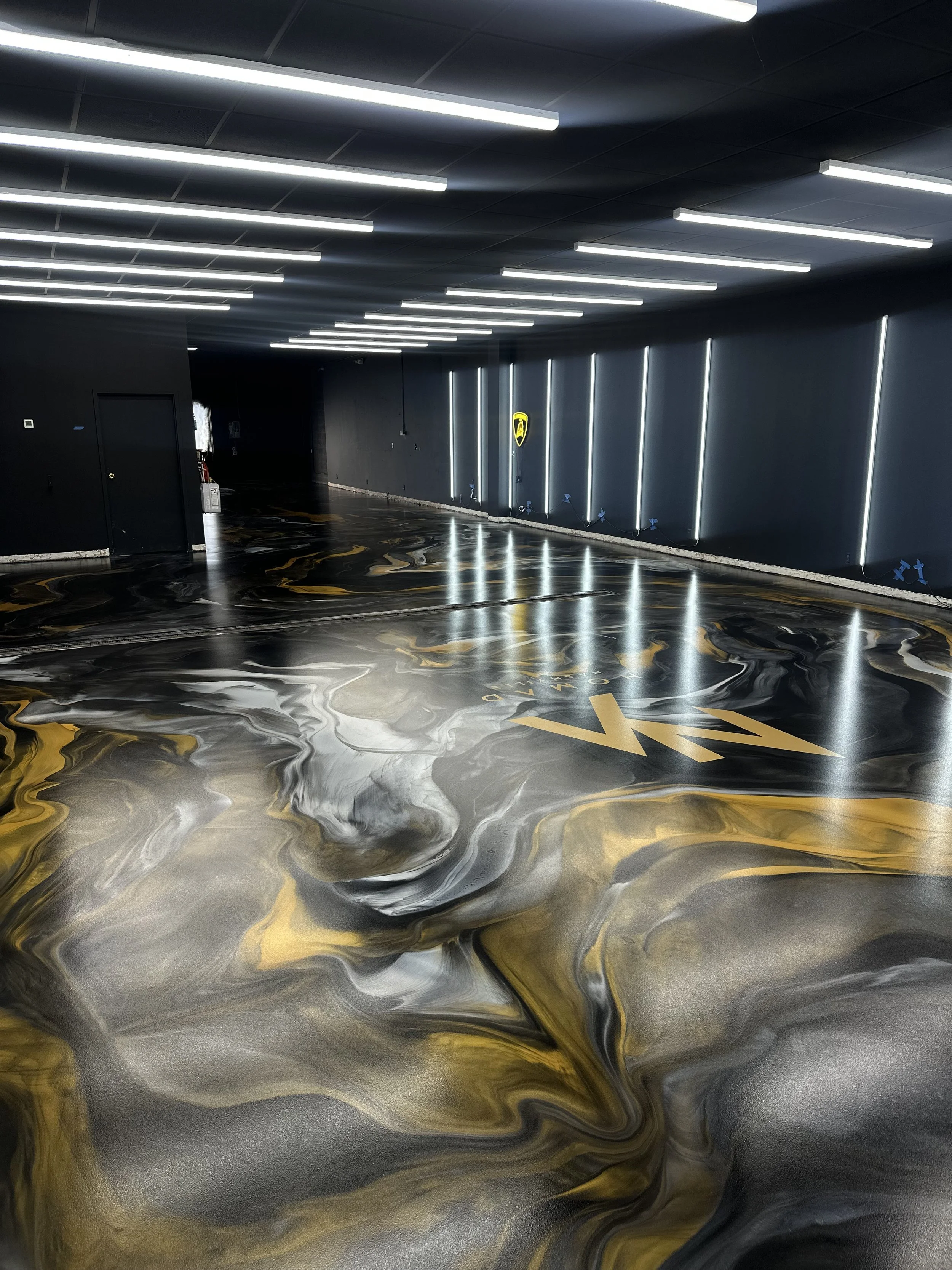 Modern parking garage with black and gold marbled floor, black walls with silver LED light strips, and bright linear ceiling lights.
