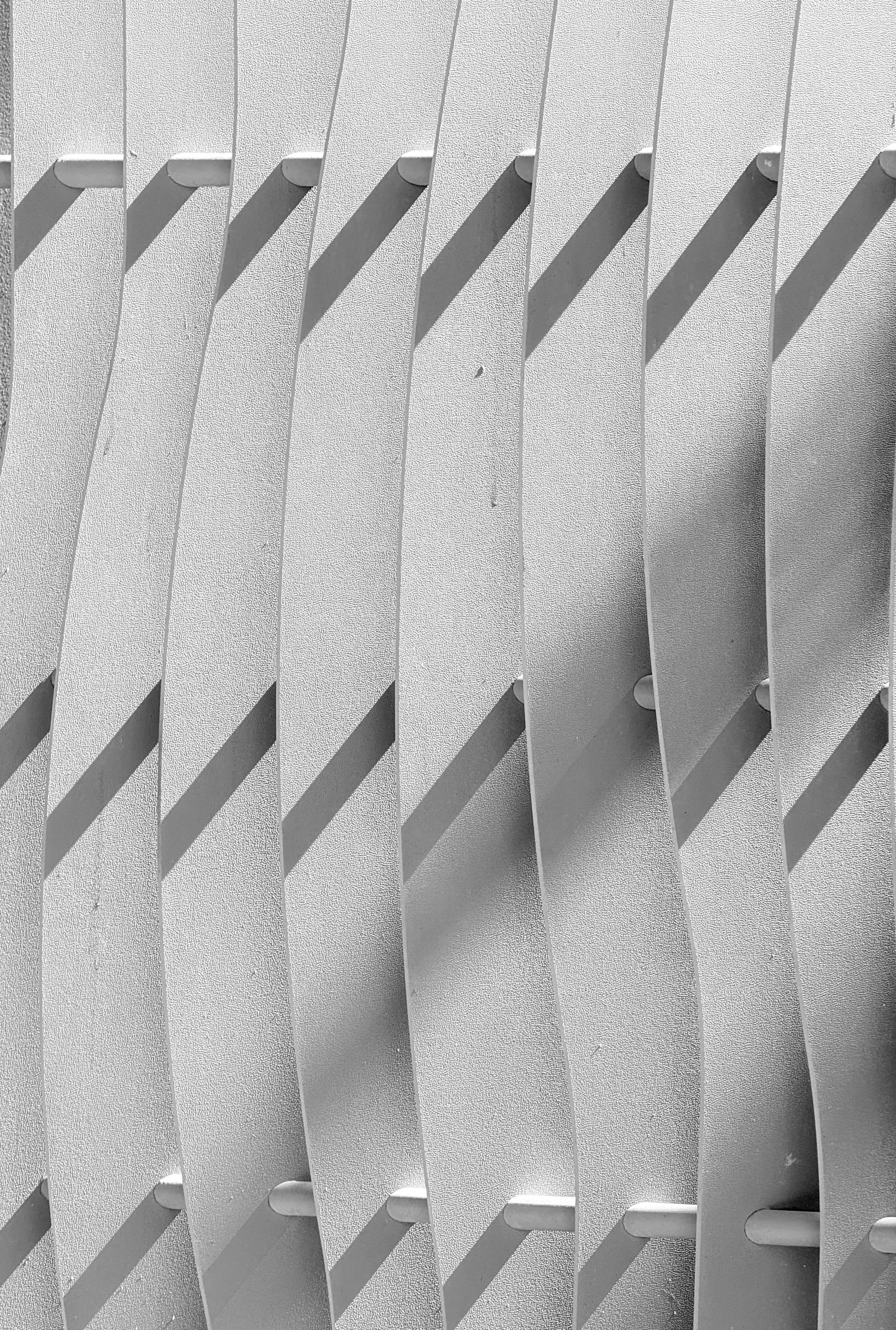Close-up of a gray, textured wall with evenly spaced, protruding horizontal slats casting shadows.