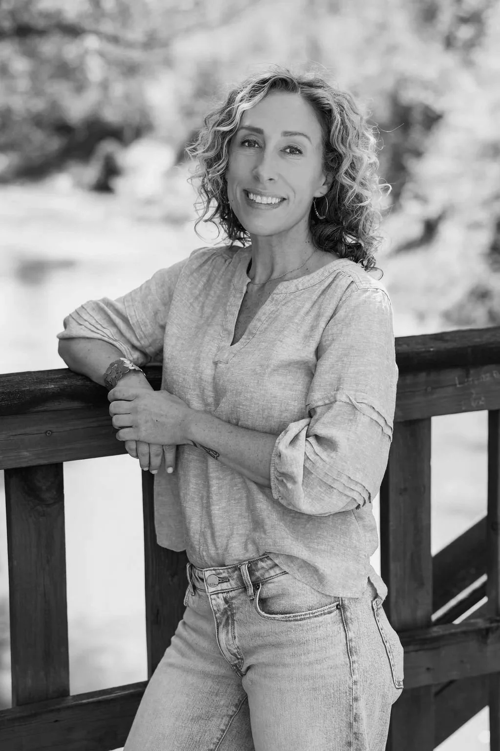 black and white headshot of a female therapist smiling while leaning against the railing of a bridge