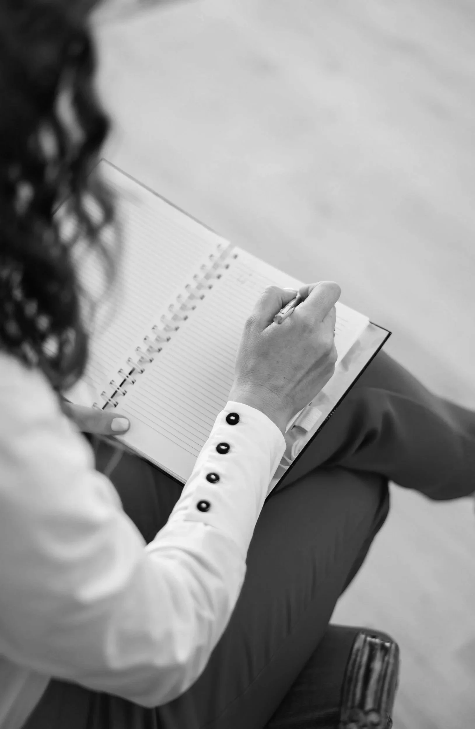 close up image looking over the shoulder of a woman therapist writing notes in a spiral bound journal