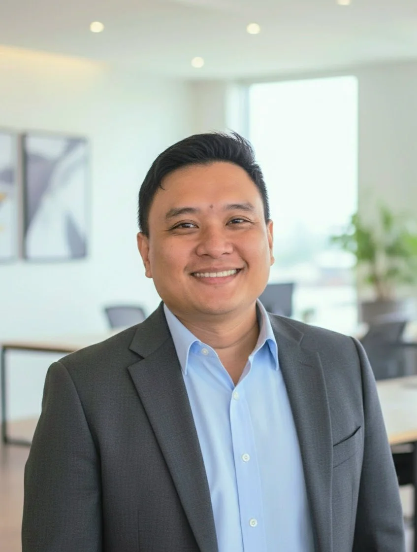 Portrait of a smiling man in business attire, standing in an office with bright natural light and modern decor.